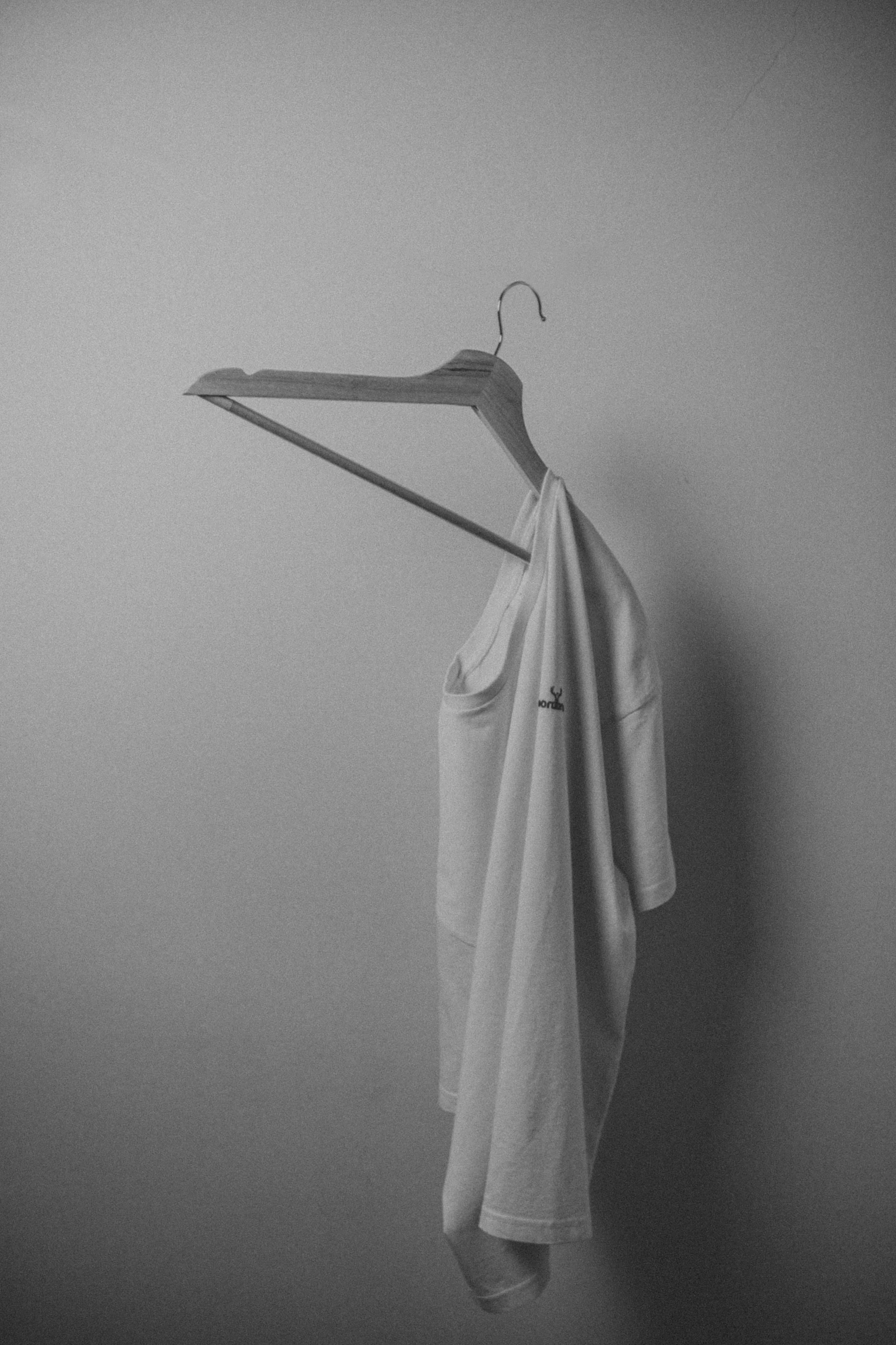 A white tank top hanging on a wooden clothes hanger suspended from a ceiling or wall hook.
