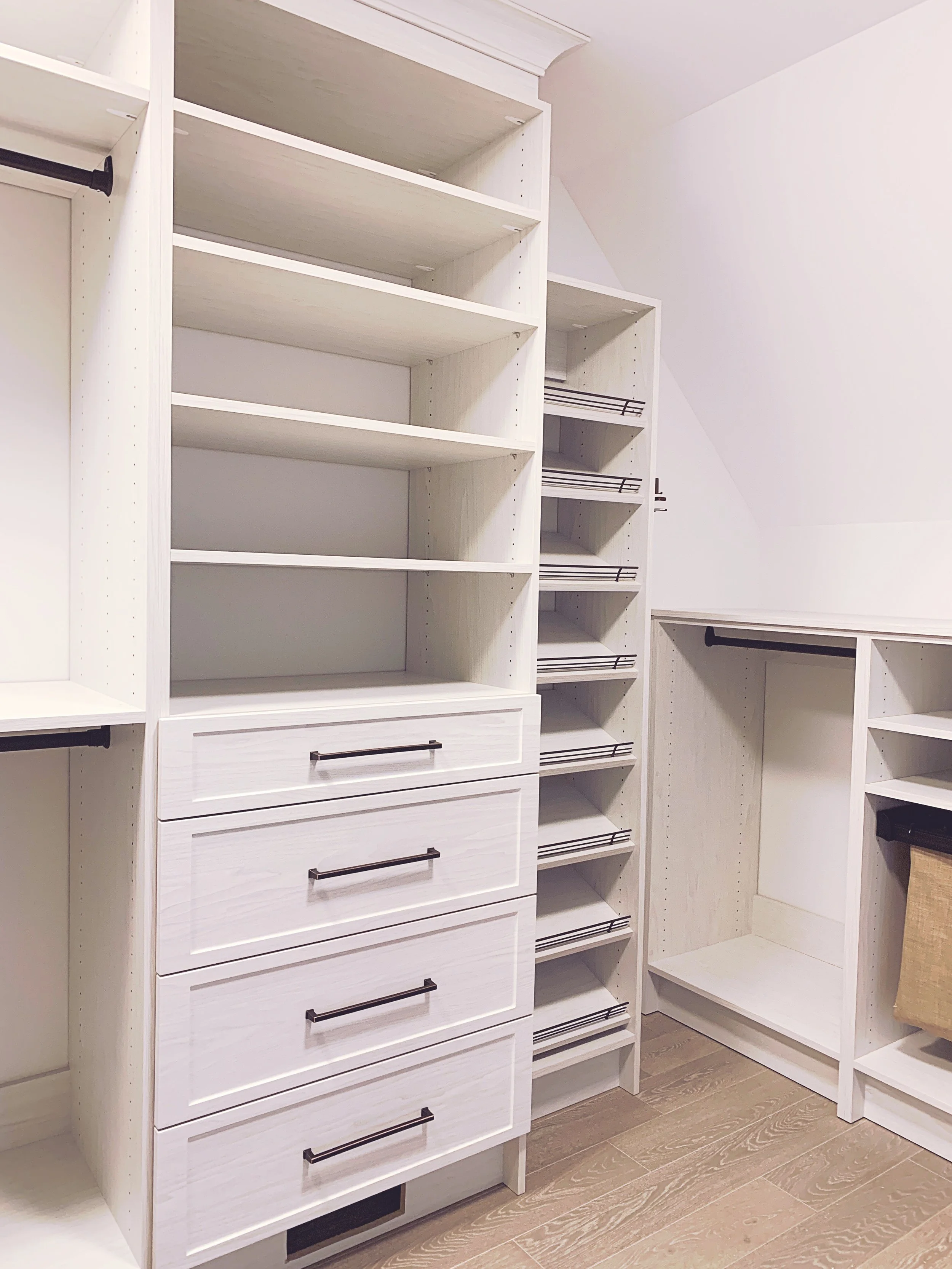 White built-in closet storage with open shelves, drawers, and hanging rods in a walk-in closet.