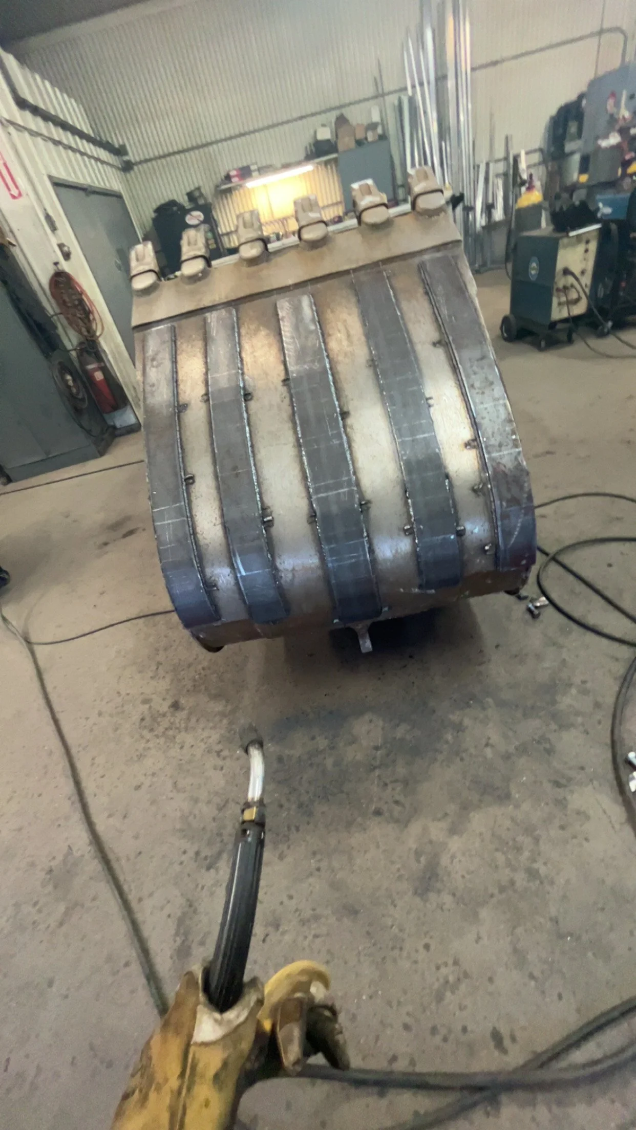 Photo of a metal object with several small white nozzles or spray tips on top, with old welding marks visible, inside a workshop with tools and equipment around.
