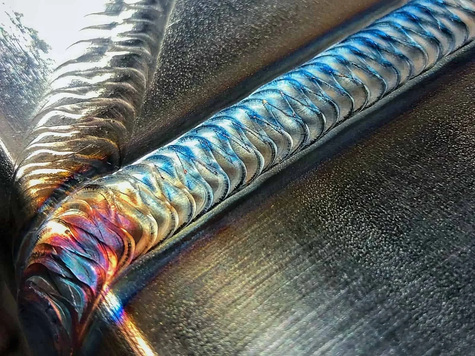 Close-up of a welded metal pipe with colorful heat marks on a dark surface.