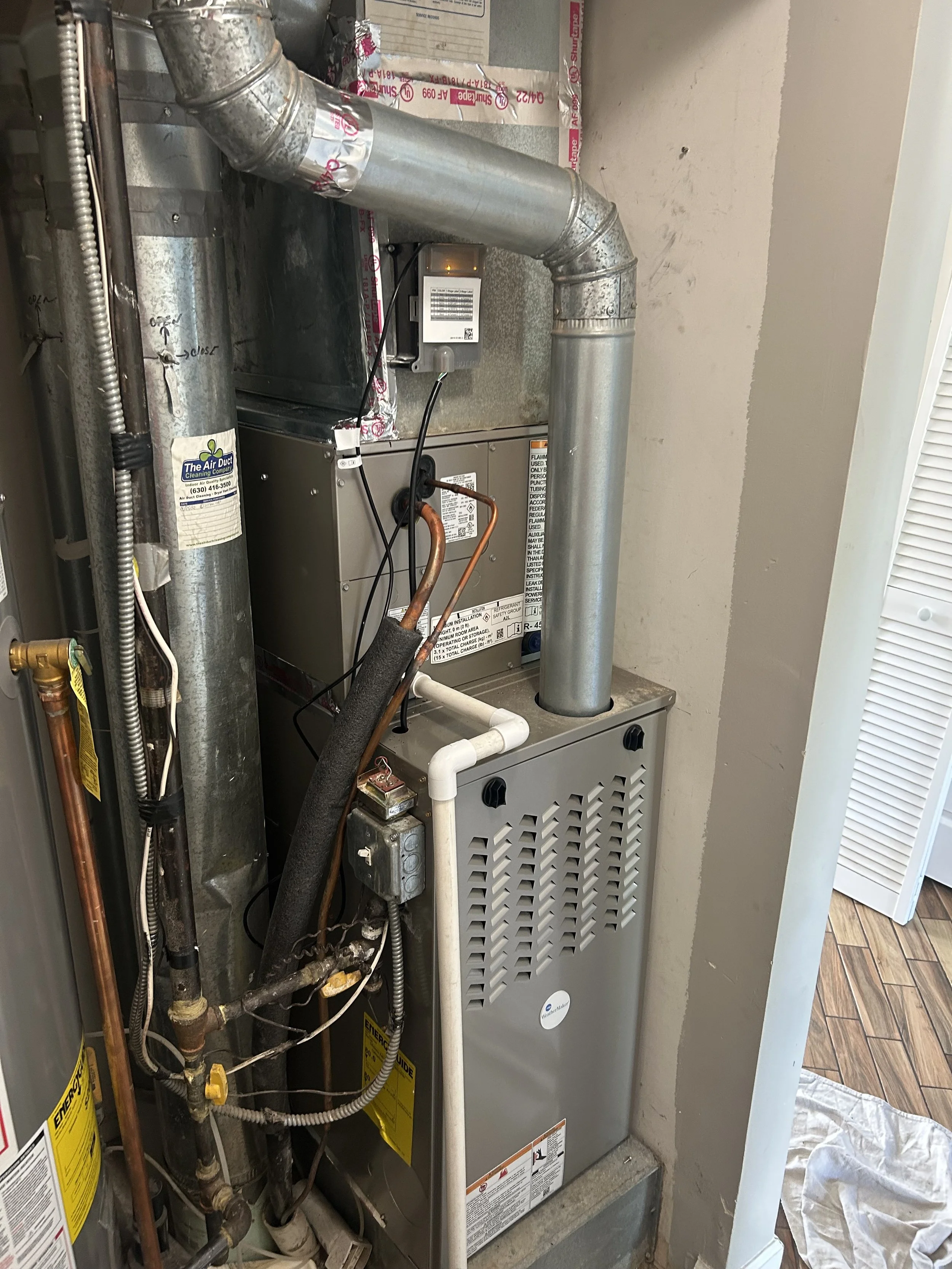 Furnace with metal ductwork and plumbing pipes in a utility room.