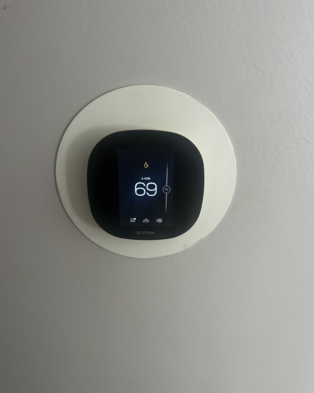 Wall-mounted smart thermostat displaying a temperature of 69 degrees Fahrenheit, set with a target of 70 degrees, on a light-colored wall.