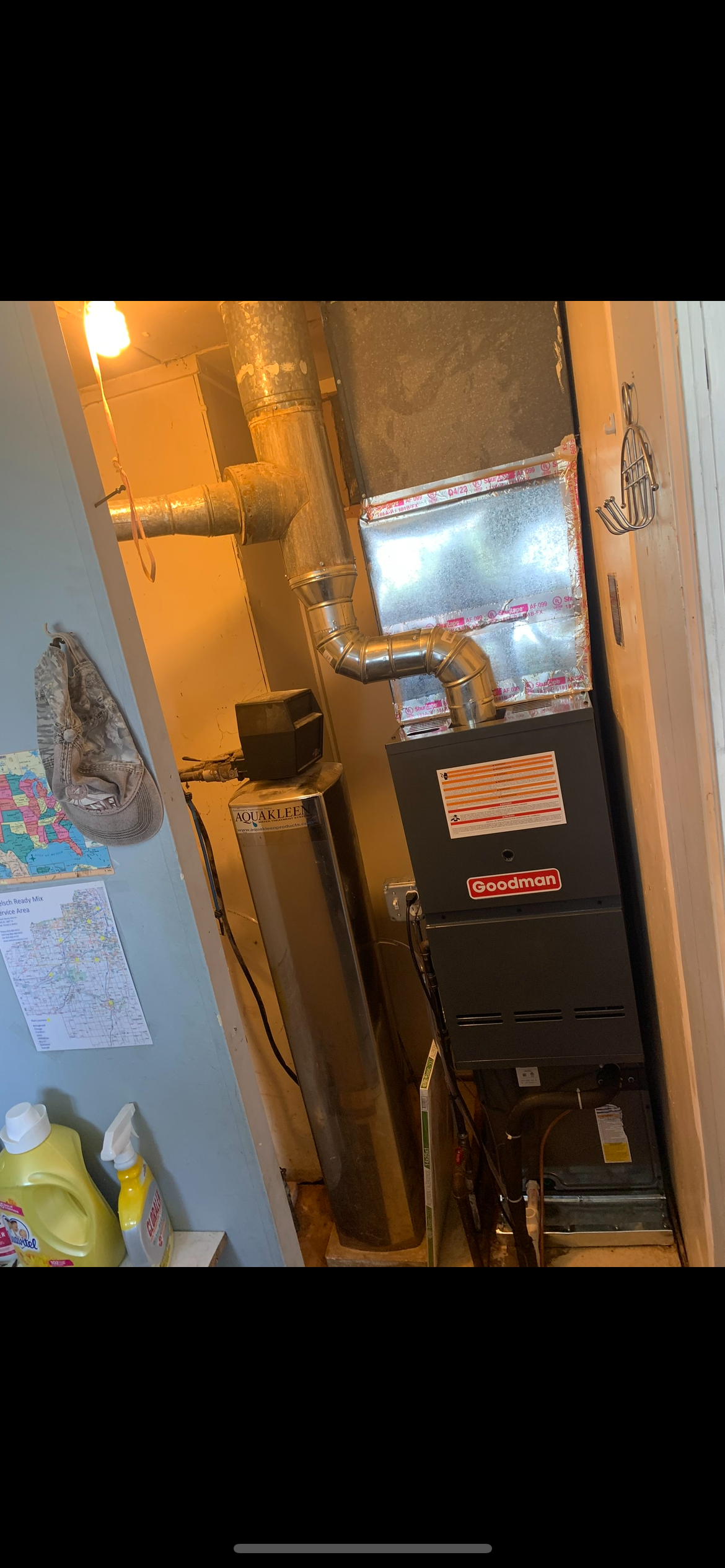 A furnace and duct system in a basement or utility room, with a yellow wall, some cleaning supplies, and maps on the wall.