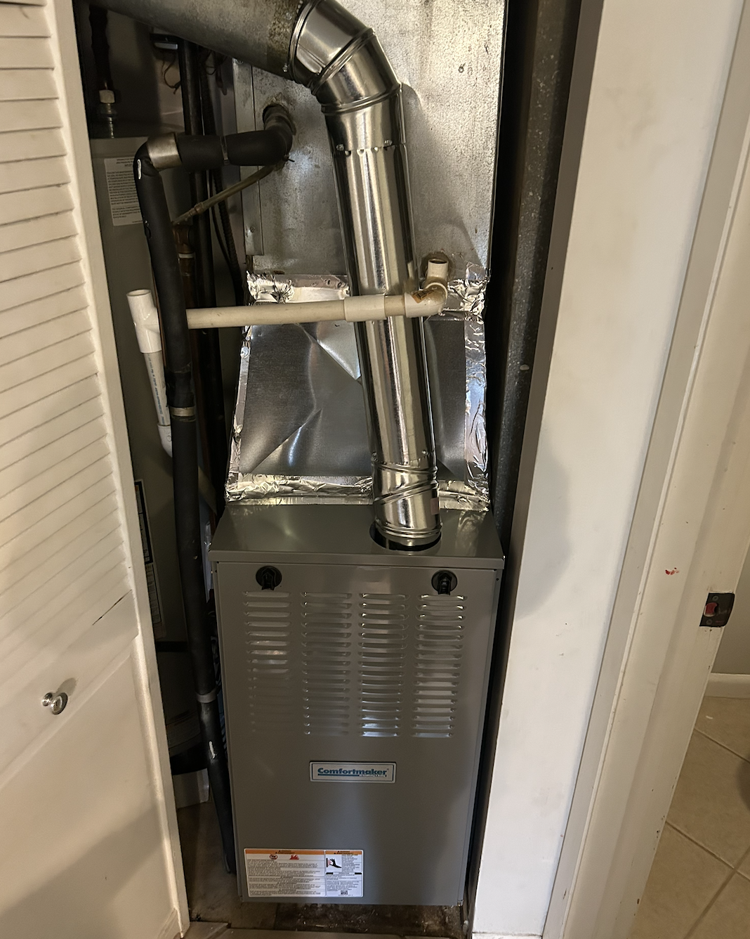 Furnace unit with metal ductwork and piping in a closet.
