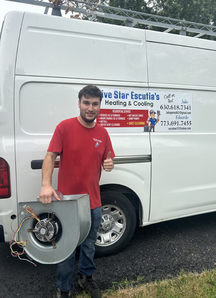 A young man in a red shirt standing next to a white work van, holding a broken furnace blower wheel with visible wires. The van has a sign promoting heating and cooling services.
