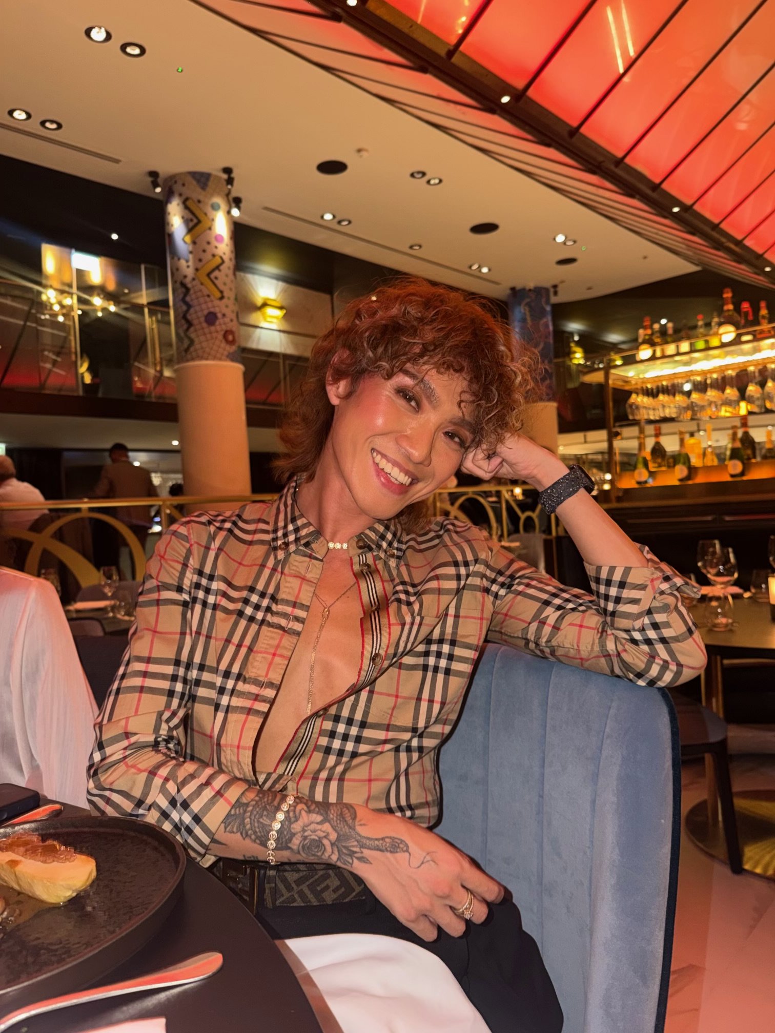 AJ Harley smiling at birthday dinner in a Burberry plaid dress shirt.
