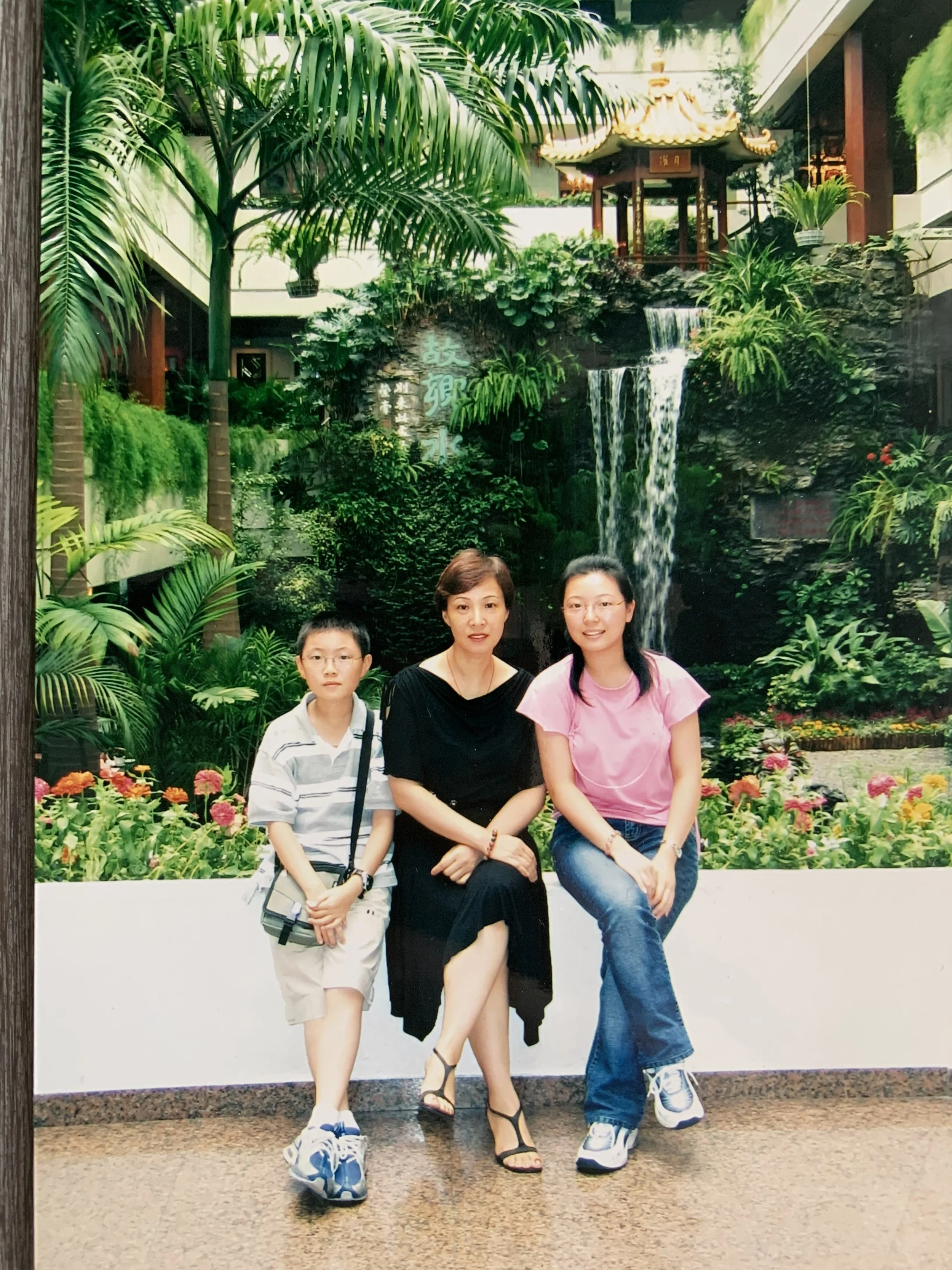 Young archival photo of AJ Harley with his mum and sister in front of a water feature showing off his mum's style in a little black dress.