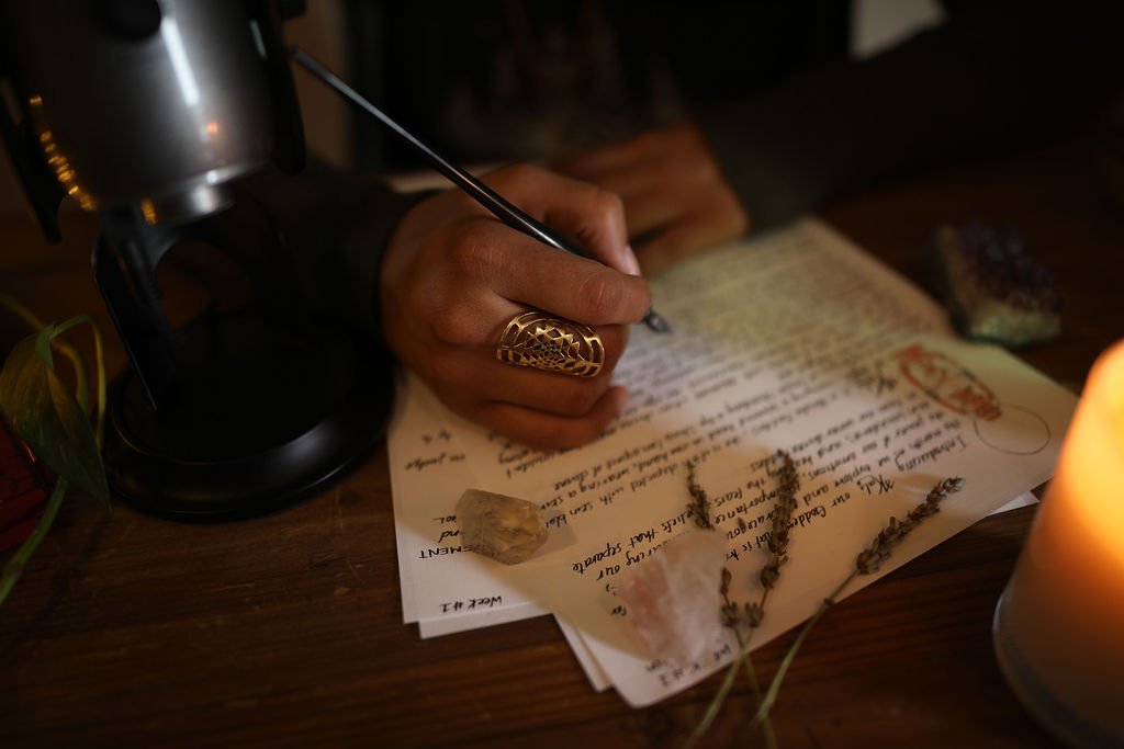 clarissa is wearing a sacred geometry ring while writing channeled wisdom on paper that also has crystals and herbs on it.
