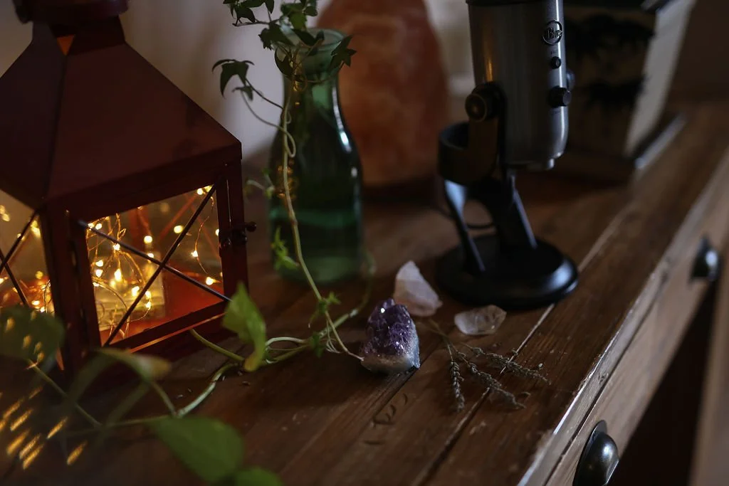 A sacred wooden altar with a lantern with fairy lights, amethyst stones, a microphone, and a beautiful ivy plant