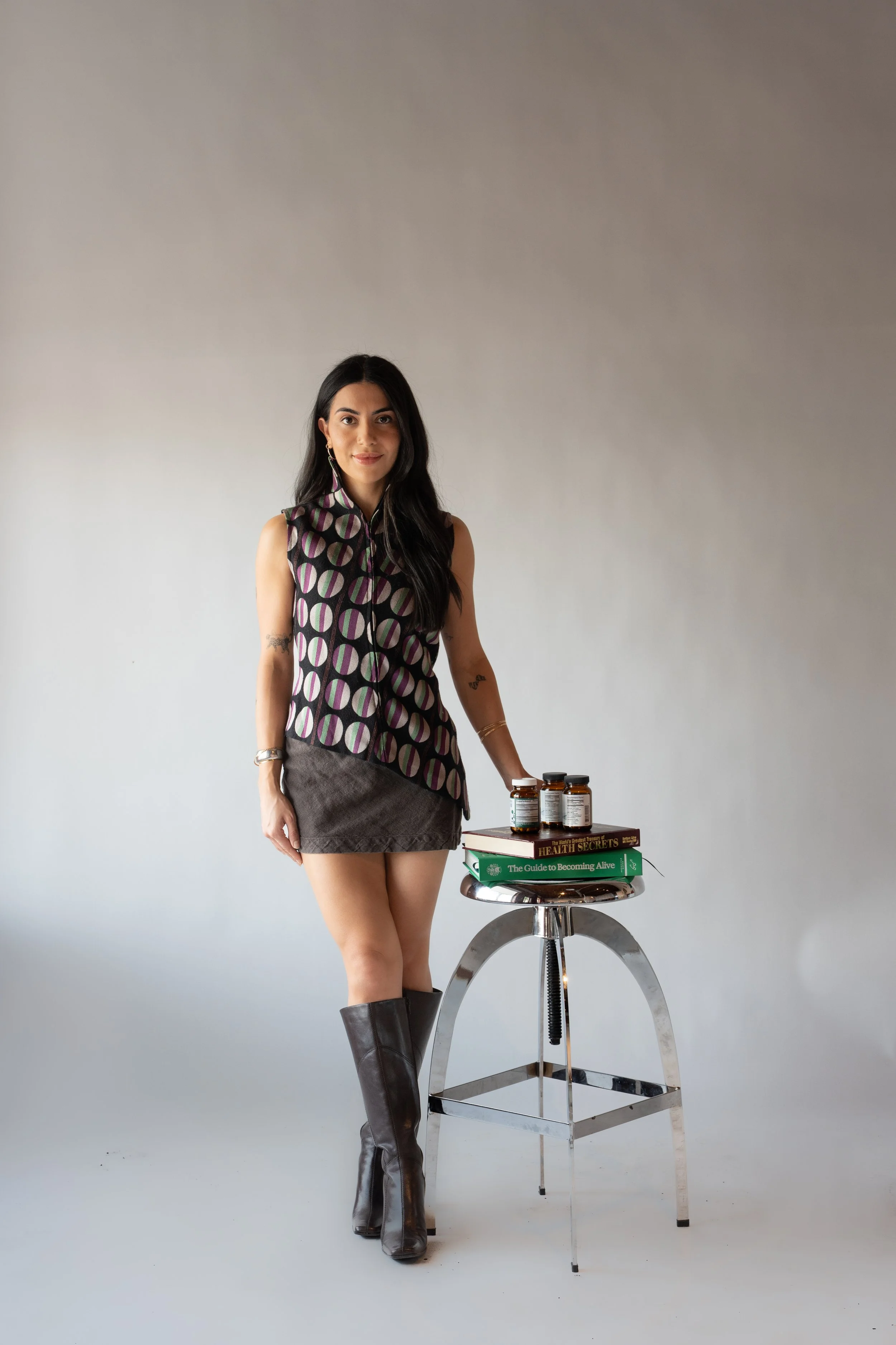 A woman standing next to a small round table with herbal supplement bottles and books on health and wellness.