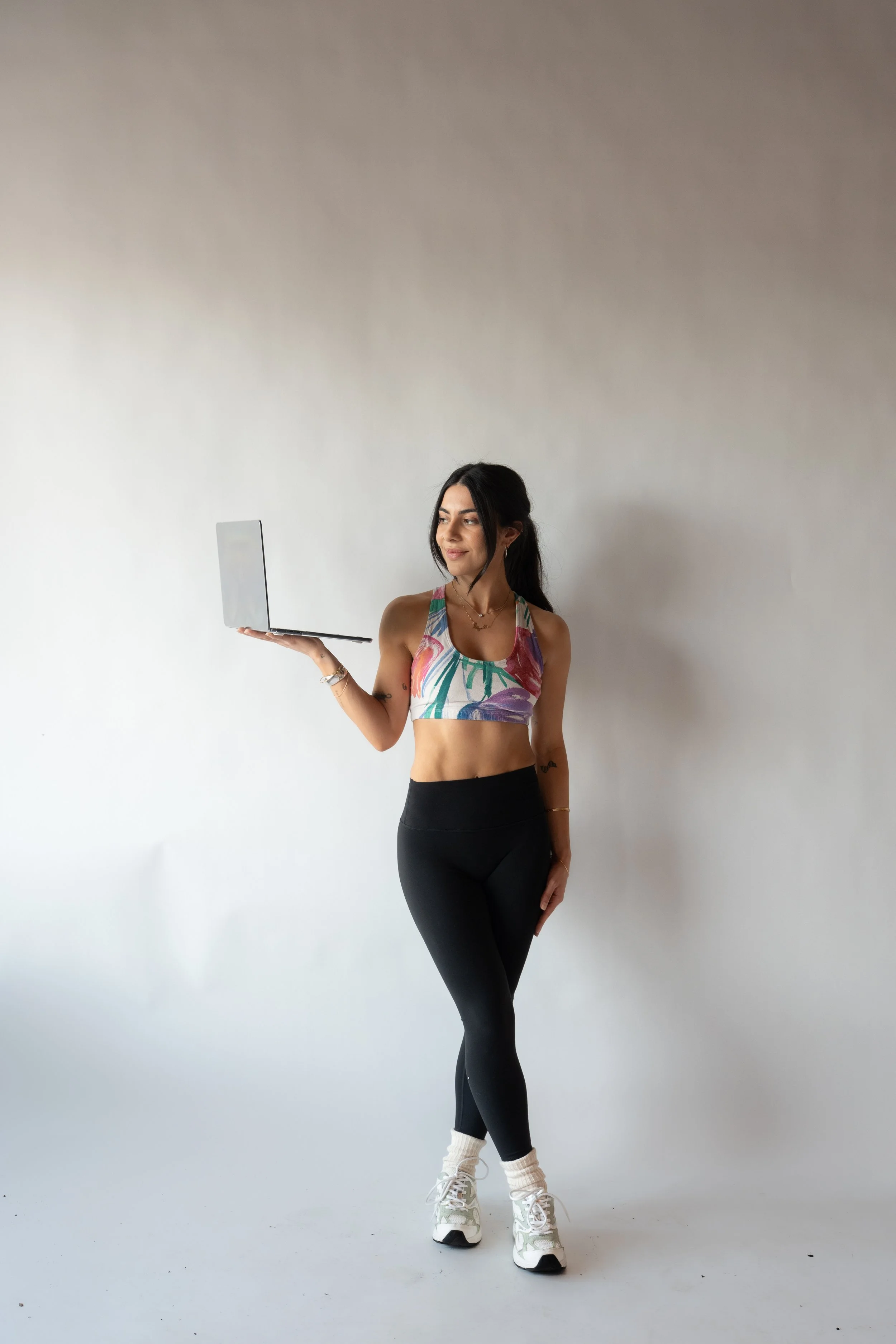 Woman in athletic wear holding a laptop in a white studio.