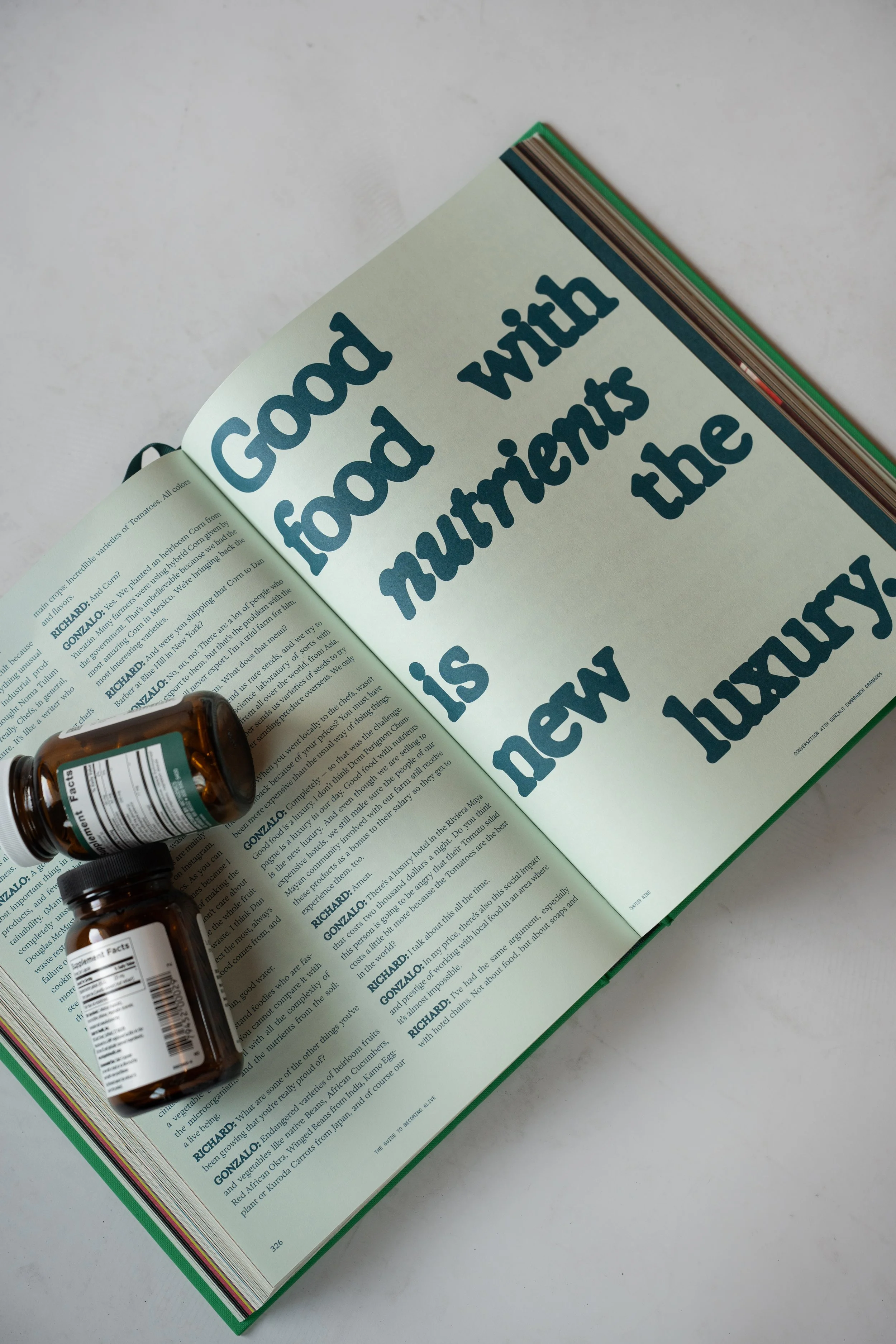 Open book with large text reading 'Good food with nutrients the new luxury' and two medicine bottles on a white surface.
