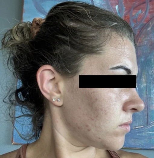 Profile of a woman with brown hair tied in a bun, wearing small earrings, standing in front of a colorful abstract painting.