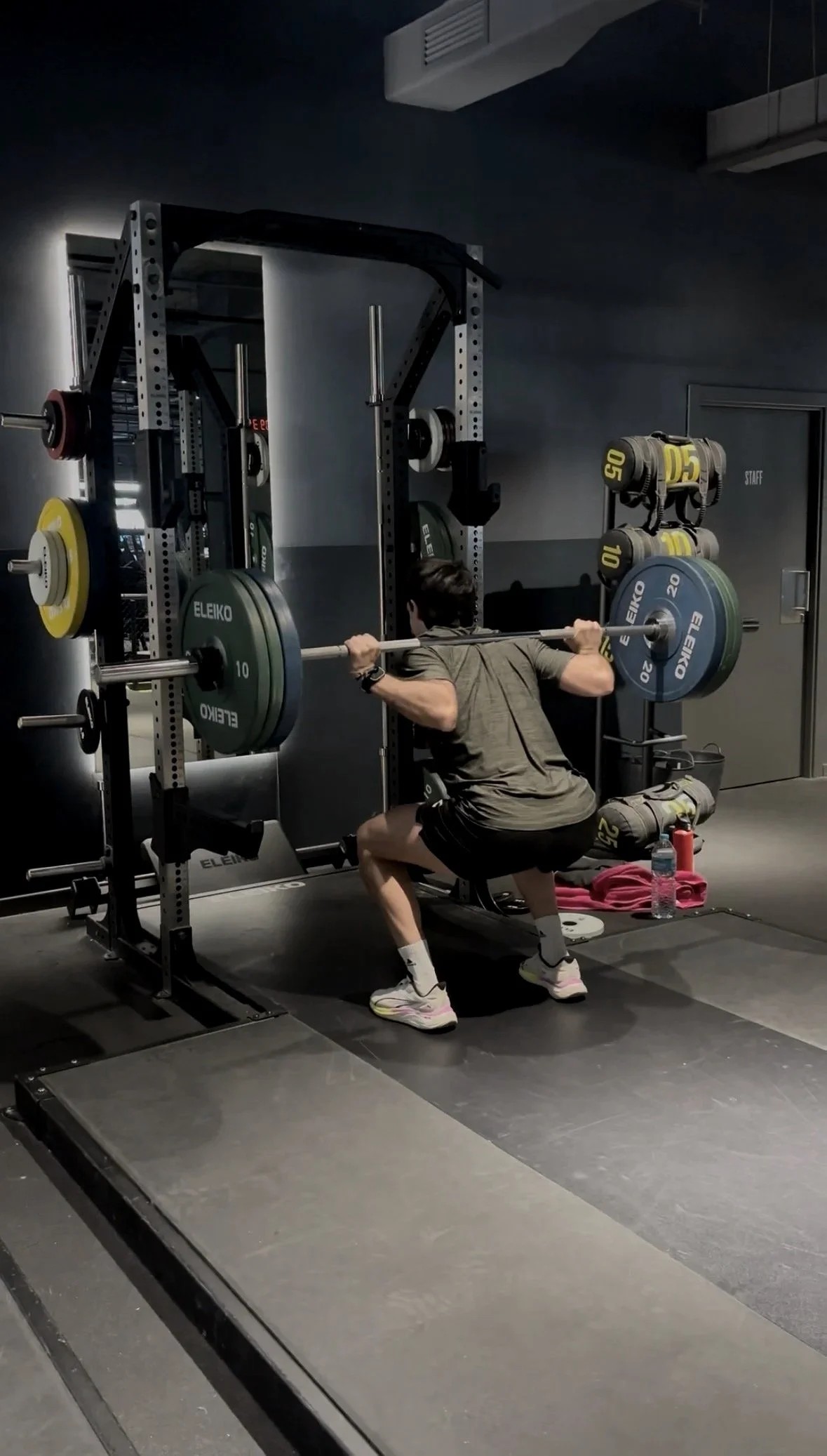 A man performing a squat exercise with a barbell loaded with colored weight plates in a gym.