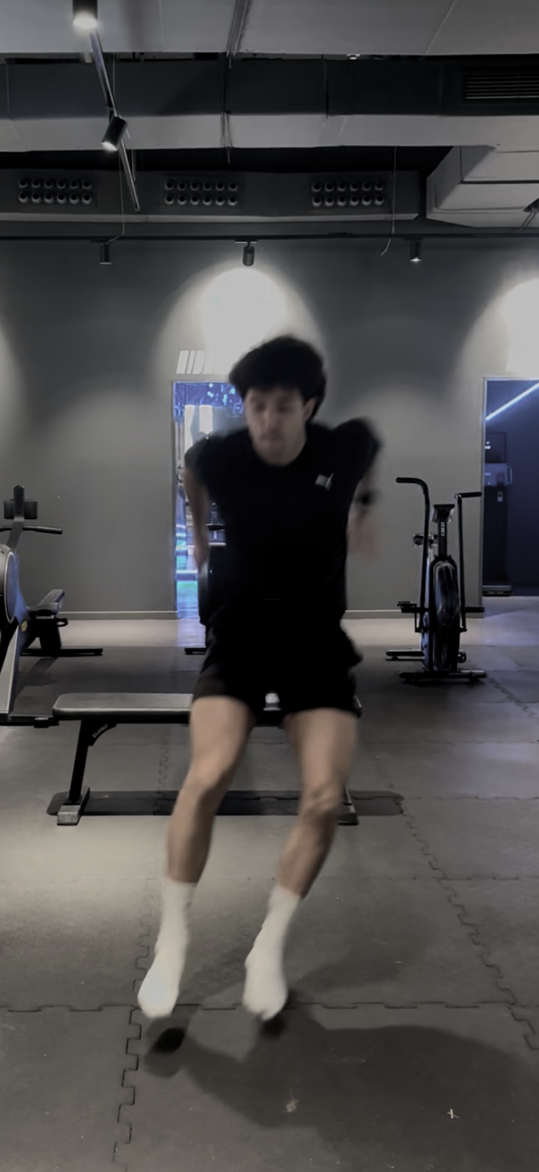 A person jumping on a trampoline or jump platform in a gym with exercise equipment in the background.