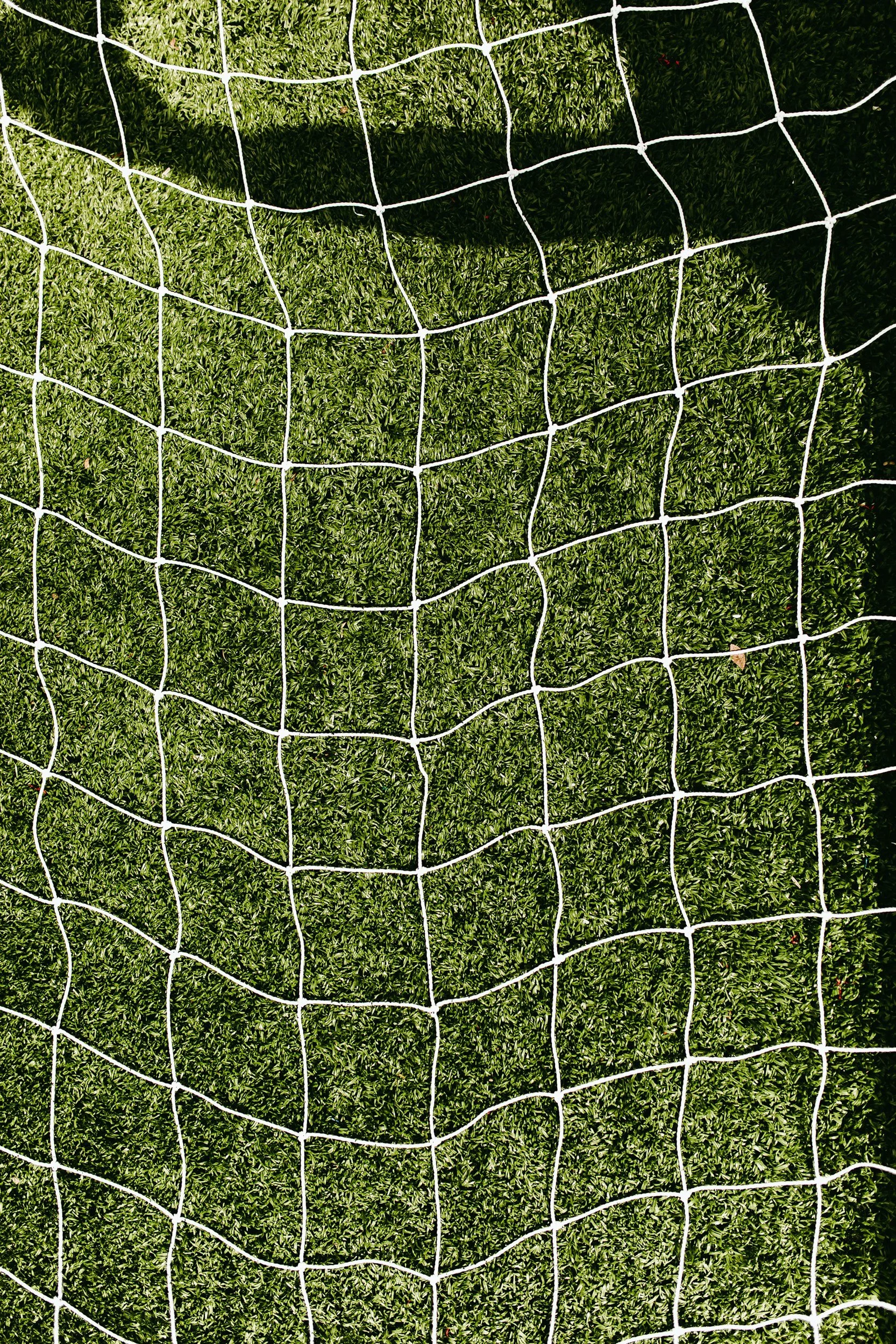 Close-up of a white soccer goal net mounted on green grass.