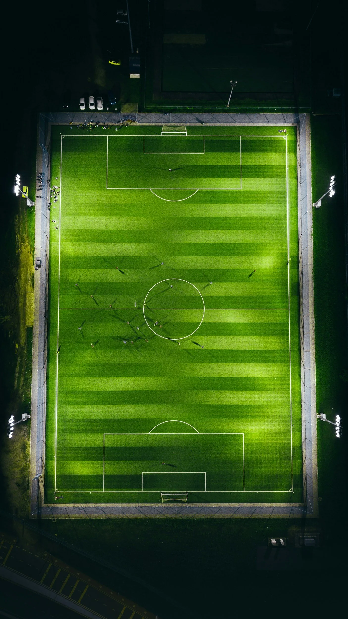 An aerial view of a brightly lit soccer field at night with players practicing on the field.