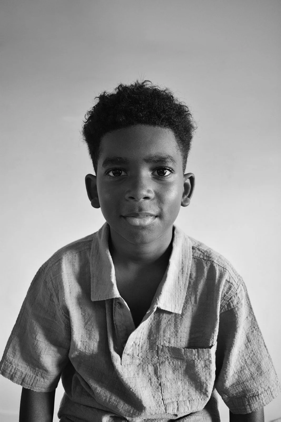 Black and white portrait of a young boy with short curly hair, wearing a button-up shirt, looking directly at the camera.