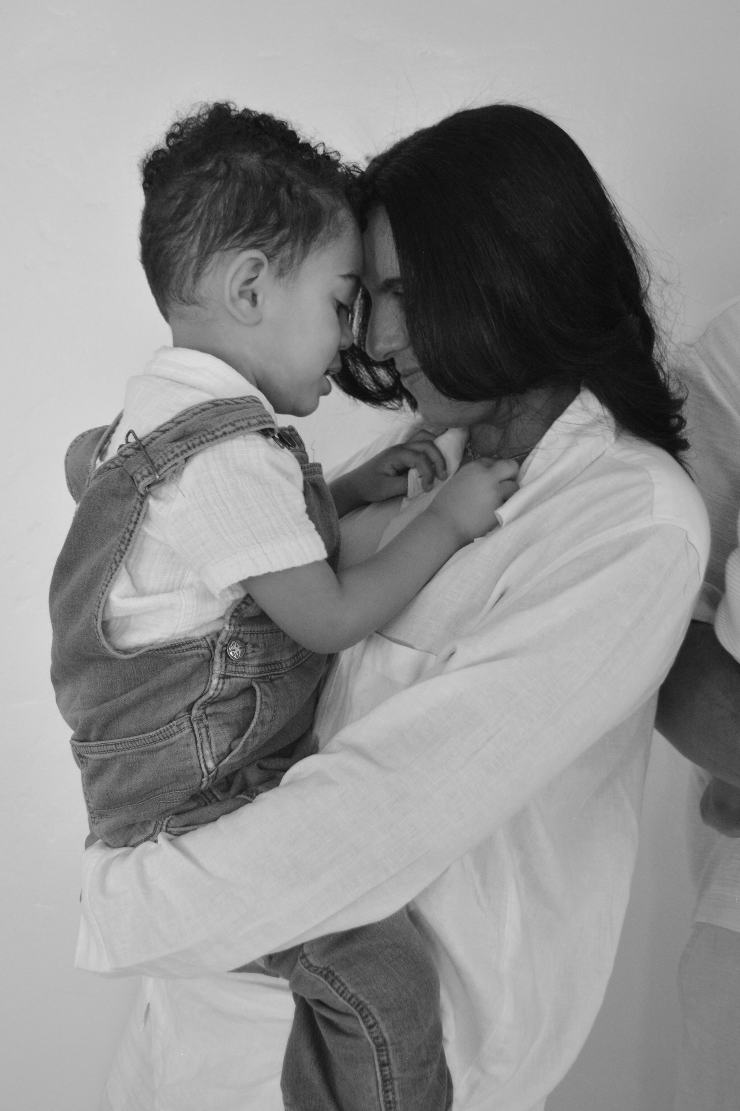 A young boy and a woman face each other with their foreheads touching. The boy is wearing a hoodie and overalls, and the woman has shoulder-length hair. They are holding hands and appear to be sharing a tender moment.