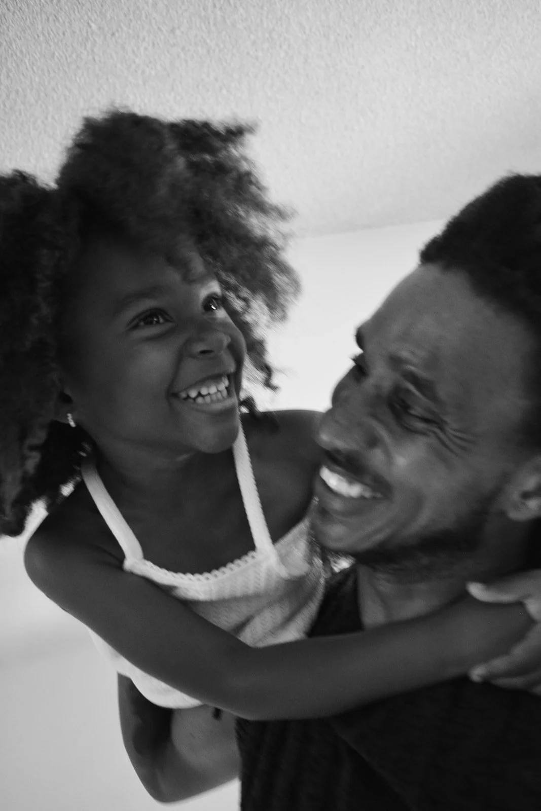 A young girl with curly hair smiling and embracing a man who is also smiling, both appear joyful.