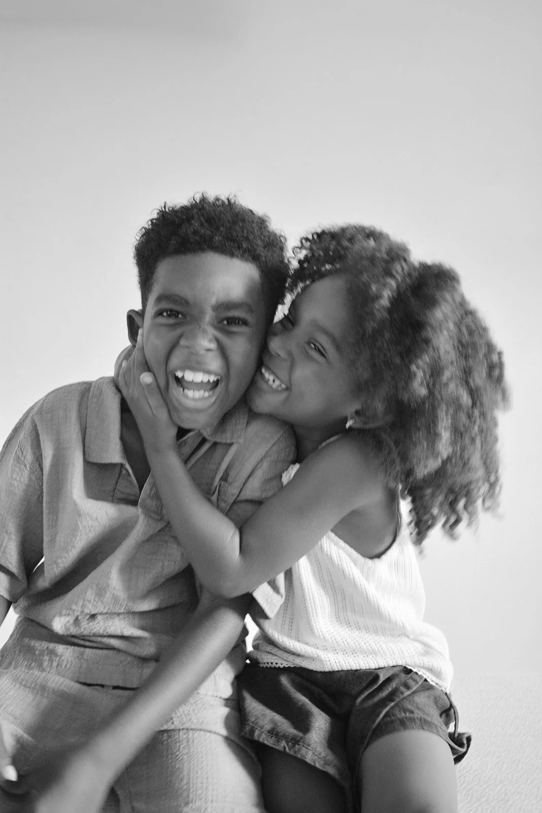 Two children, a boy and a girl, sharing a joyful moment, smiling and laughing, with the girl hugging the boy.