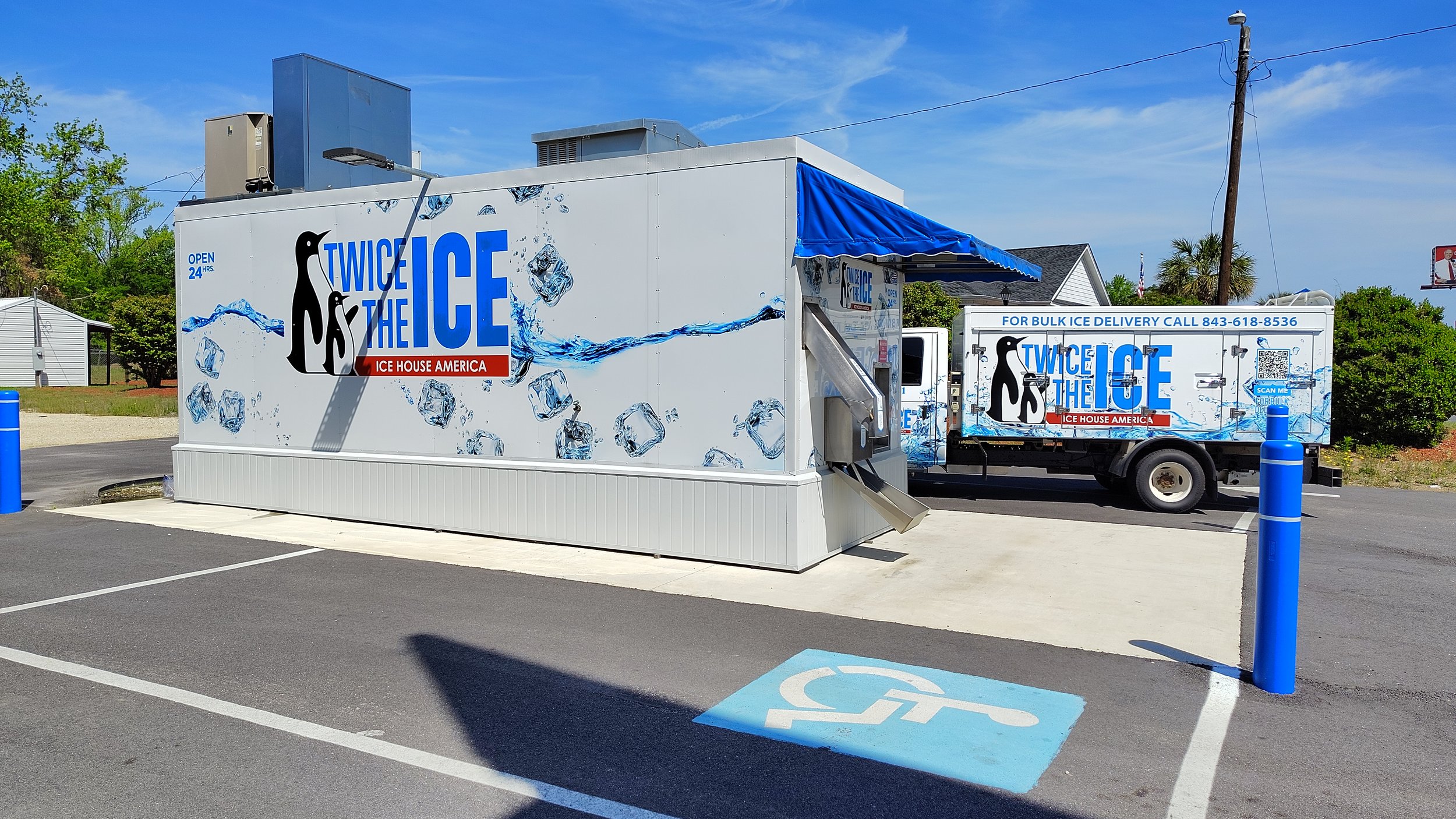 A ice house and a delivery truck, both decorated with ice-themed graphics and the logo "Twice the Ice" in blue and black, parked in a lot near a handicap parking space marked with blue paint and a wheelchair symbol.