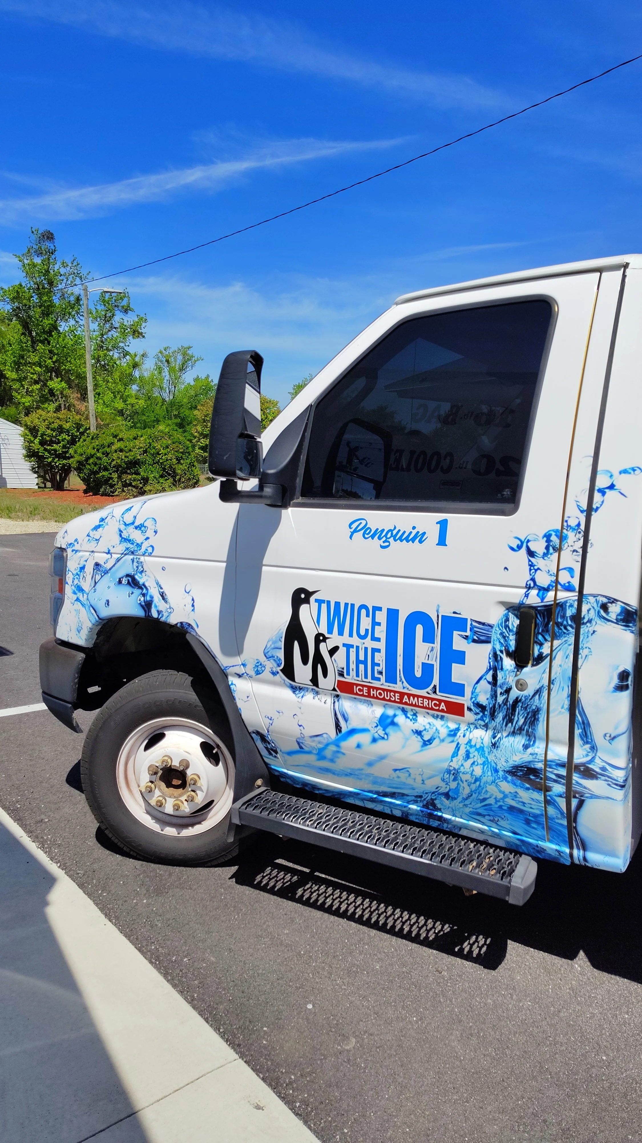 A truck decorated with an ice and water theme, featuring the words 'Twice the Ice' and 'Penguin 1' on its side, parked on a sunny day.
