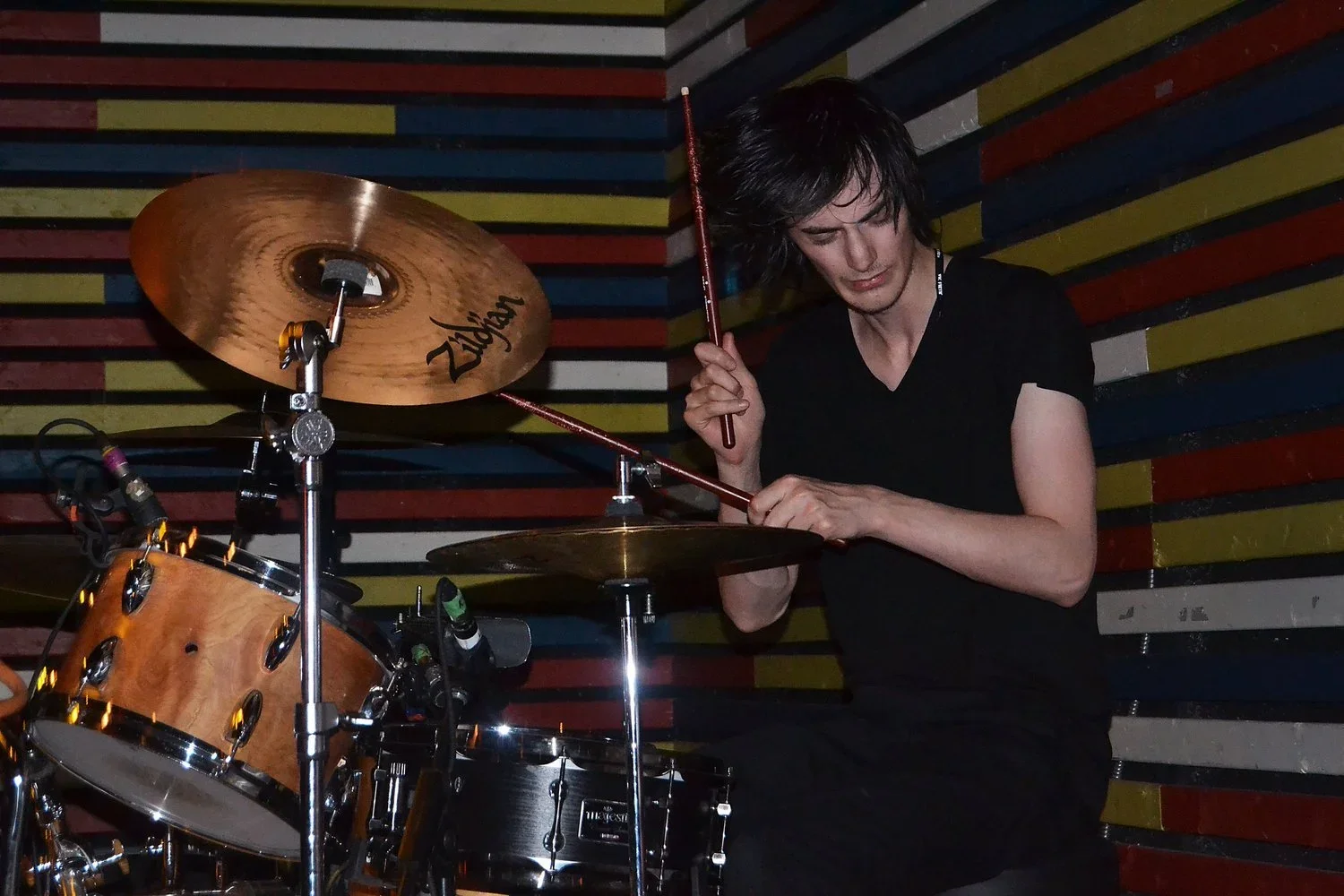 A person playing drums in a colorful wooden wall background.
