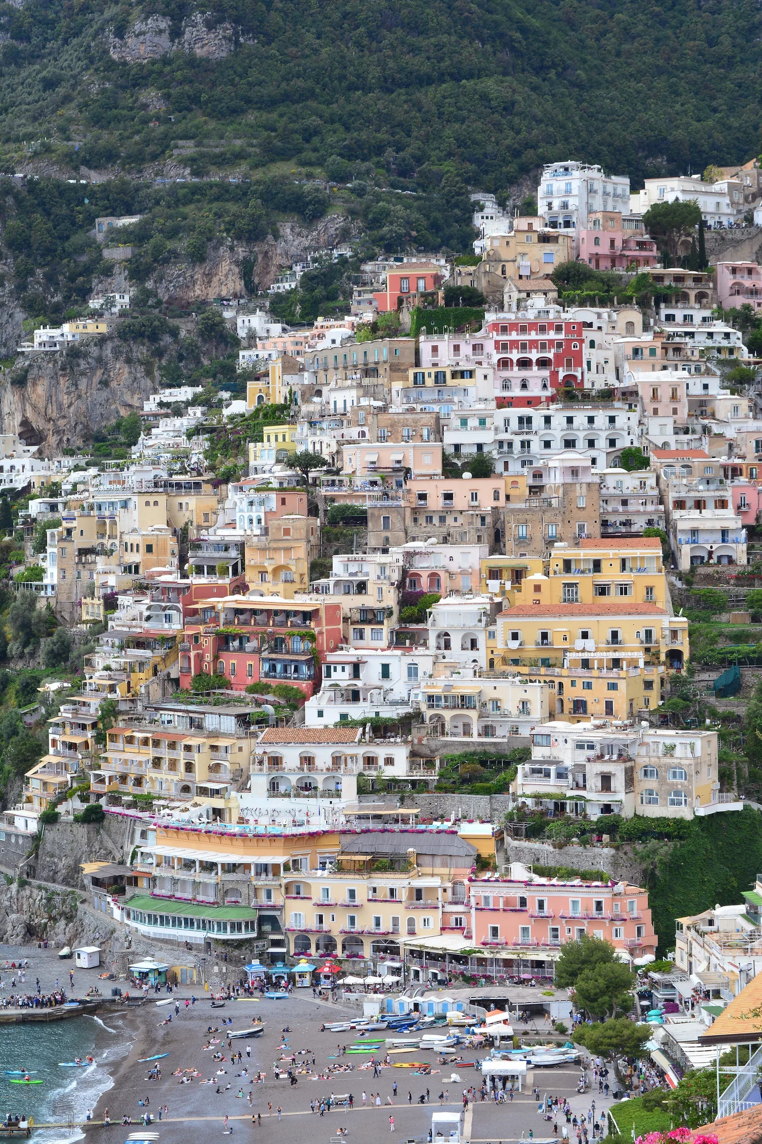 Colorful buildings on a steep hillside overlooking a beach with people and boats.