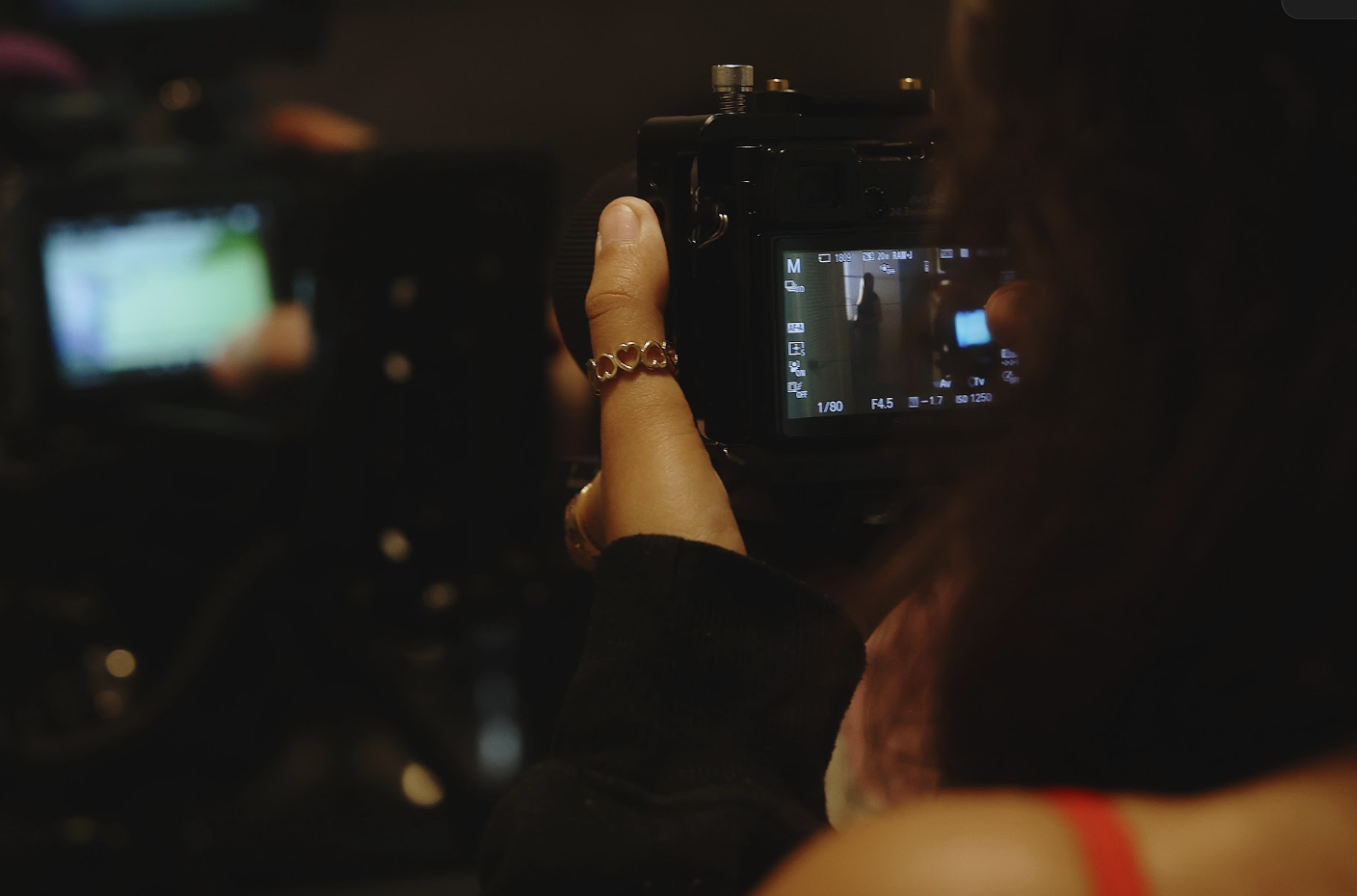 Person taking a photo with a digital camera, focusing on the camera's display screen in a dimly lit environment.