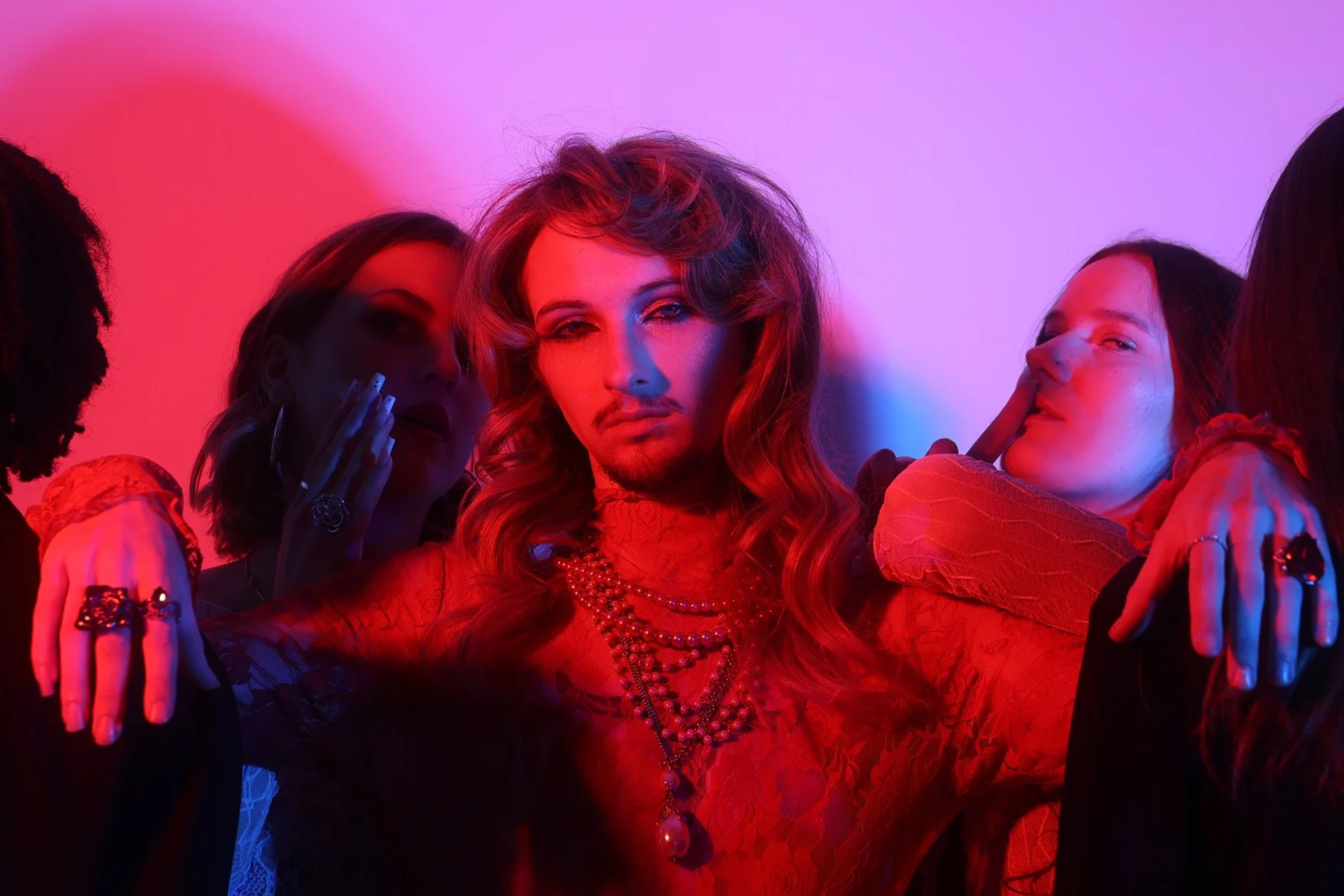Group of women surrounding a woman with wavy hair and jewelry, illuminated by colorful red and purple lighting.