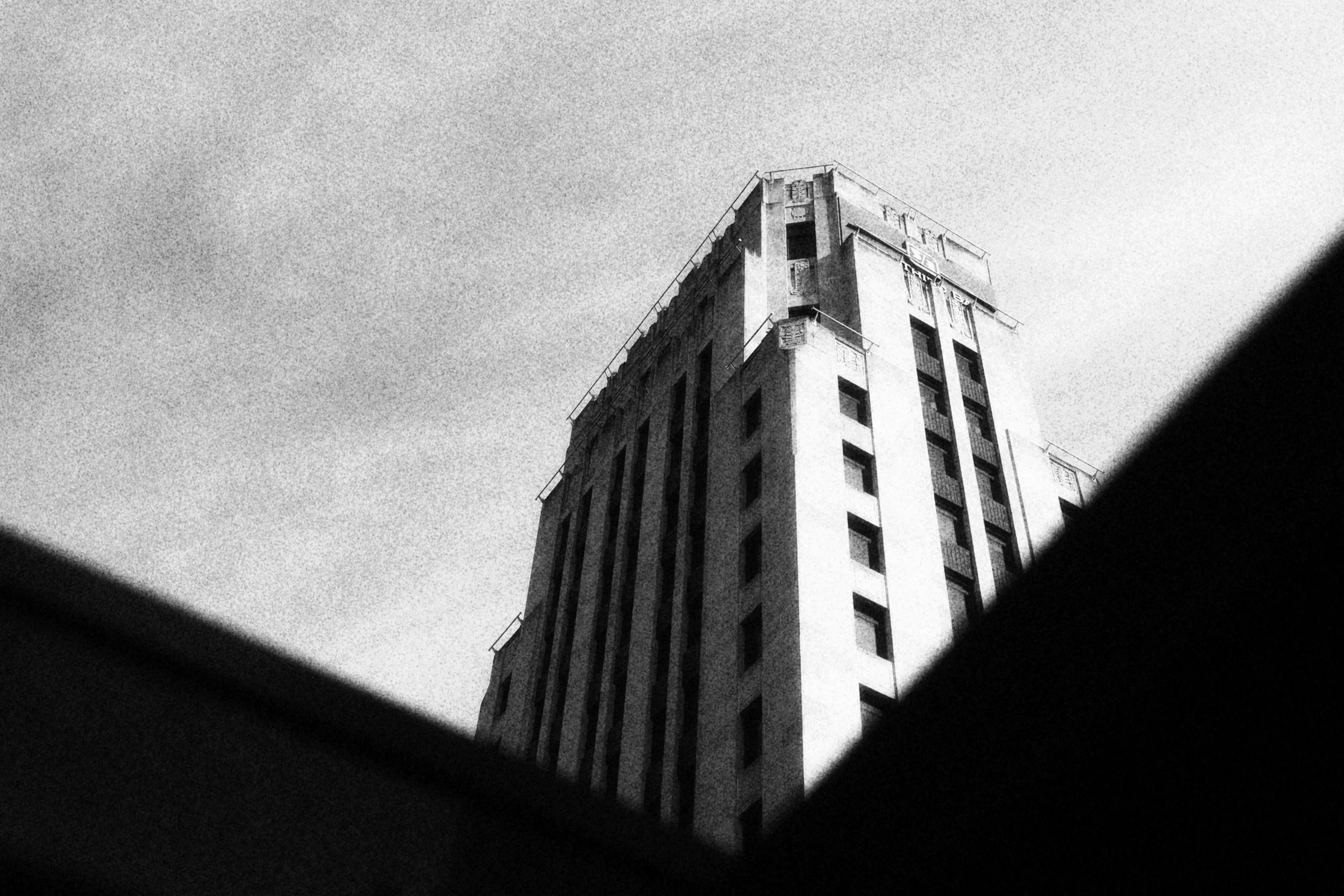 Black and white photo of a tall building taken from a low angle, with textured shadows framing the image.
