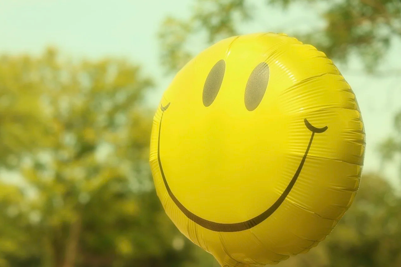Yellow smiley face balloon outdoors with trees and sky in the background.
