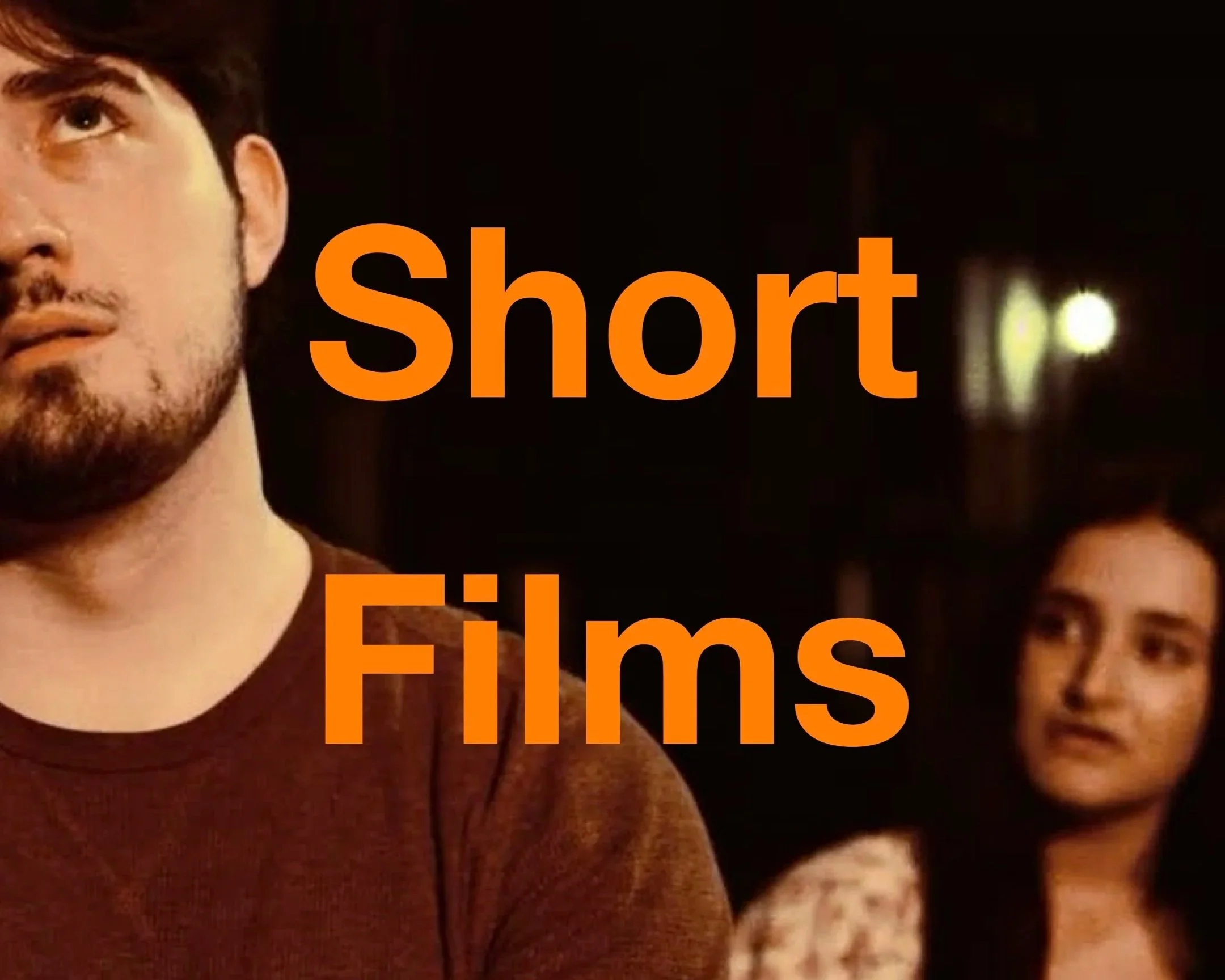 Close-up of a young man's face with dark hair and beard, next to a young woman's face with long dark hair, both with serious expressions, overlaid with orange text reading 'Short Films'.