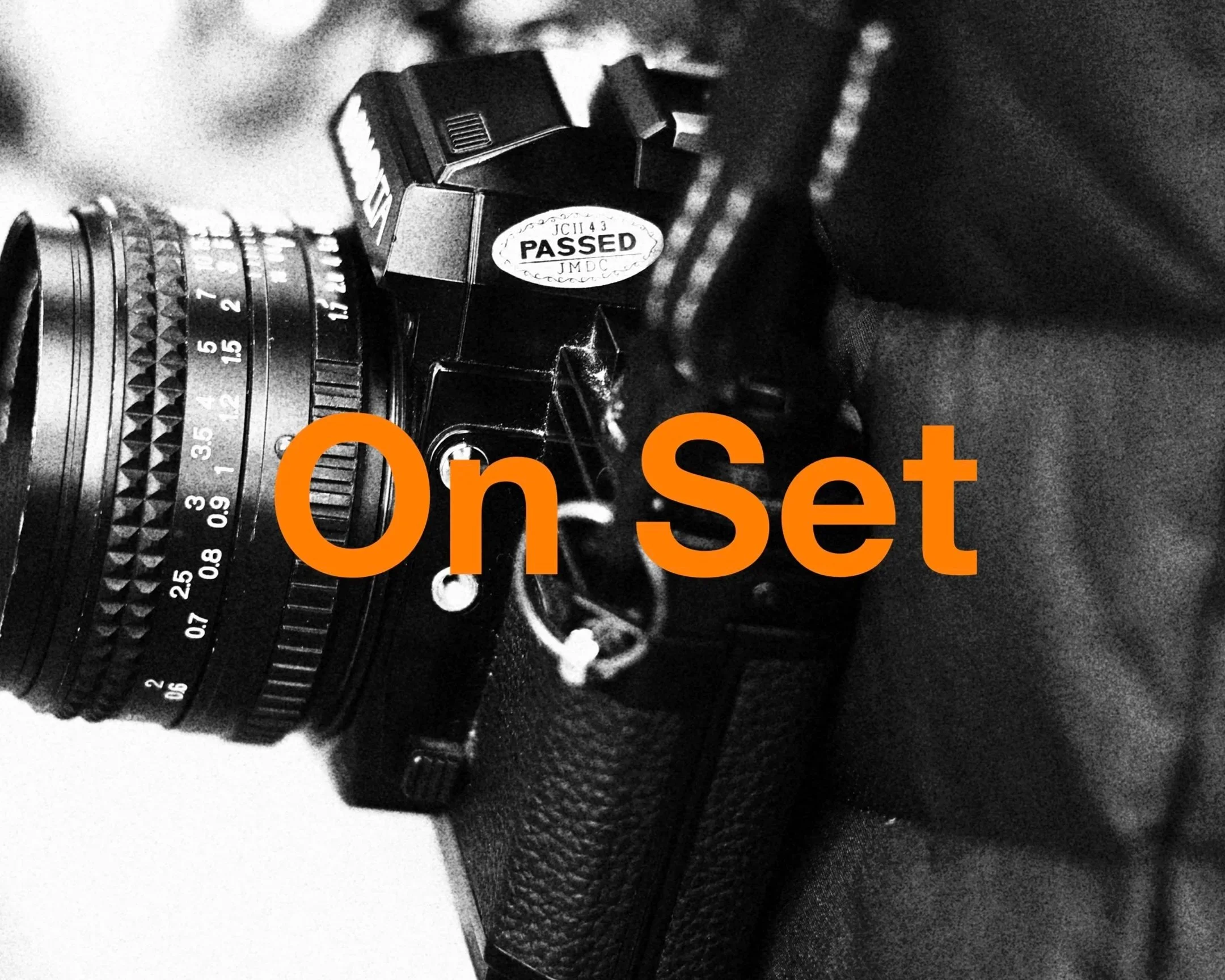 Close-up photo of a vintage camera lens with a 'Passed' sticker attached to the camera body, partially covered by large orange text reading 'On Set'.