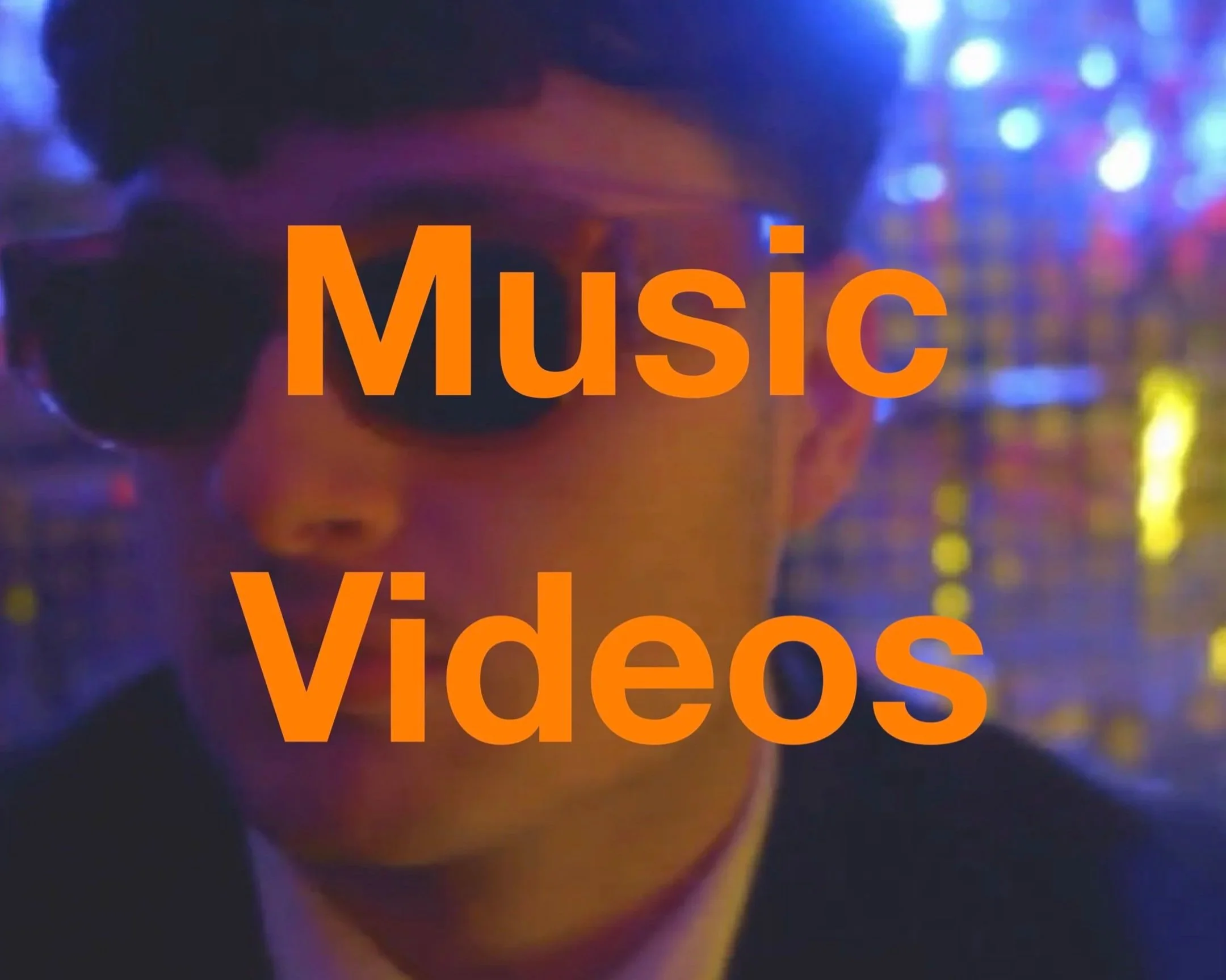 Close-up of a person wearing headphones and sunglasses, with colorful lights in the background, overlaid with the words 'Music' and 'Videos' in bold orange text.