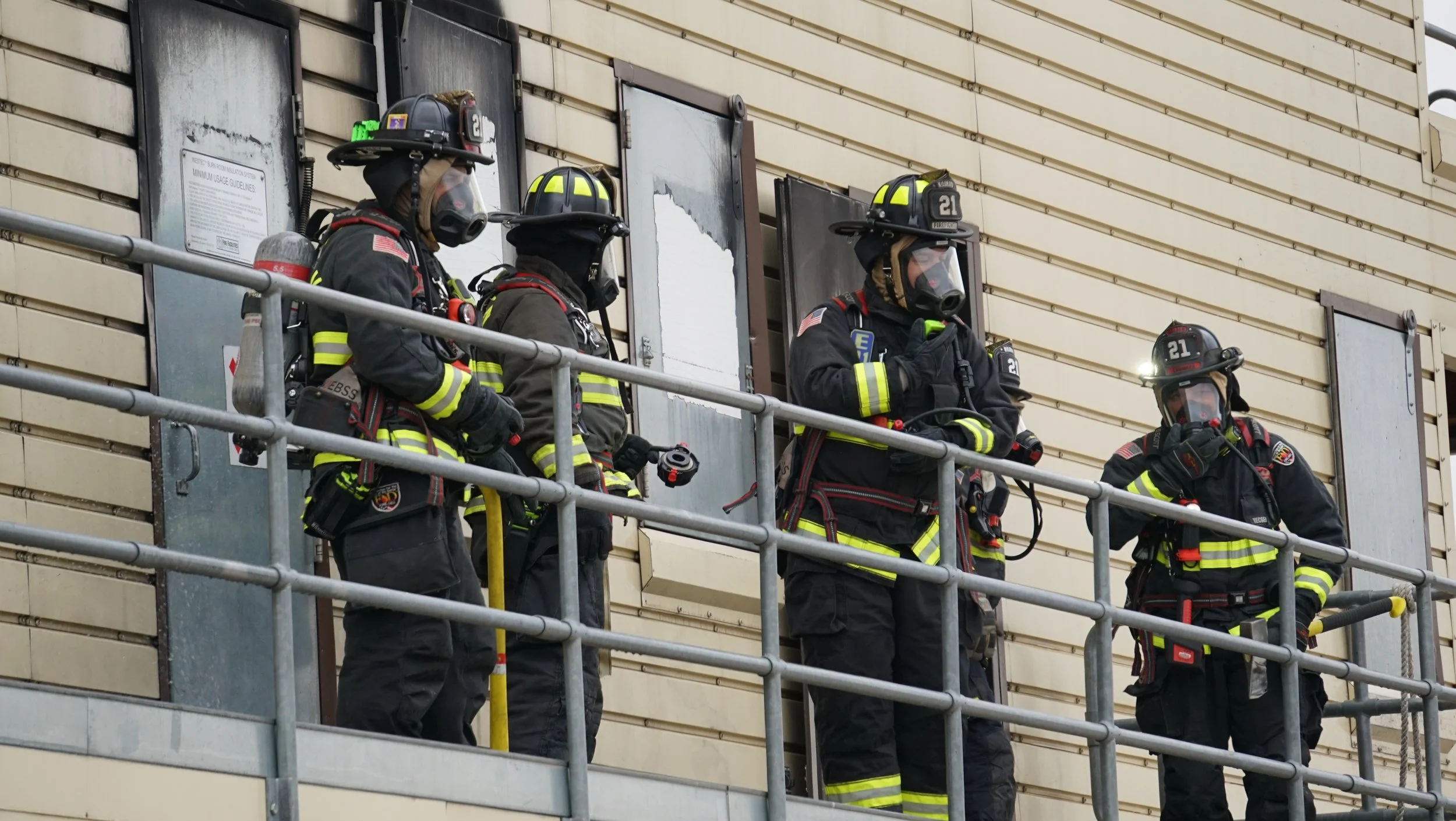 Four firefighters in full gear on a balcony, looking outward with serious expressions.