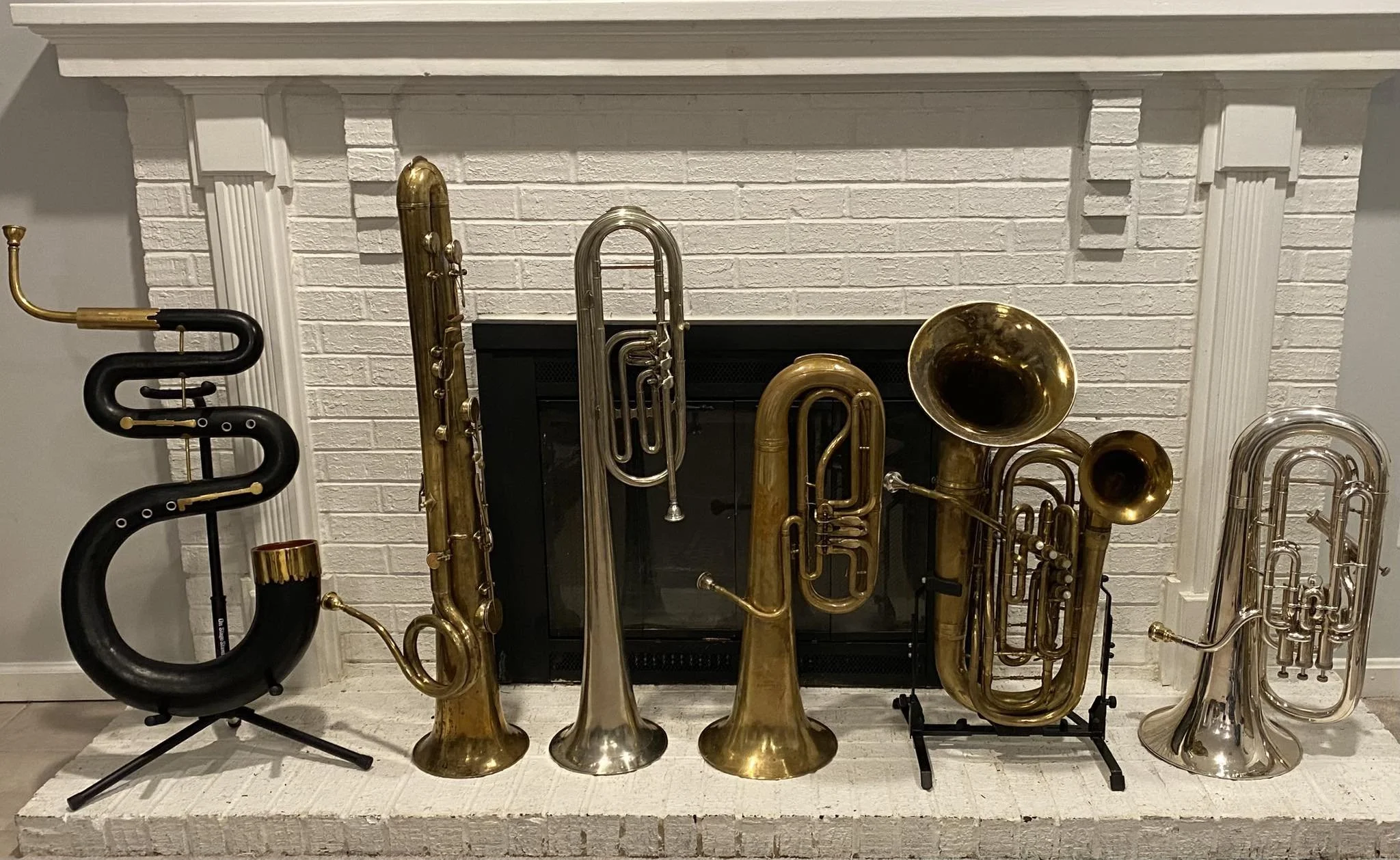 Collection of six musical brass and wind instruments arranged on a white brick fireplace mantel.