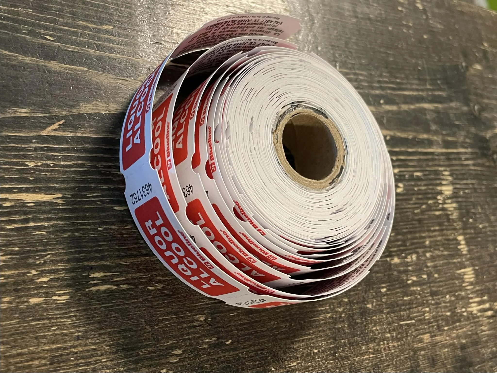 A roll of red and white adhesive labeling stickers on a wooden surface.