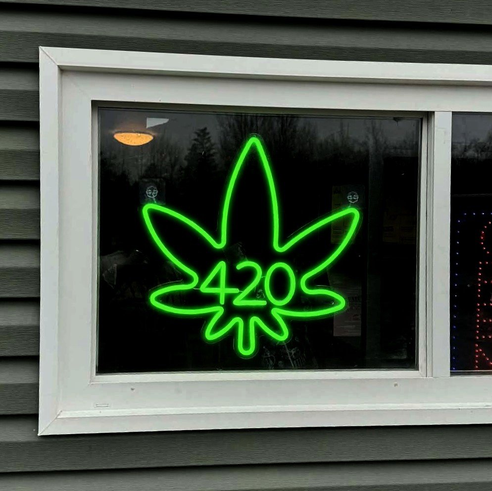 Green neon sign in the shape of a cannabis leaf with the numbers 420 inside it, displayed in a window.