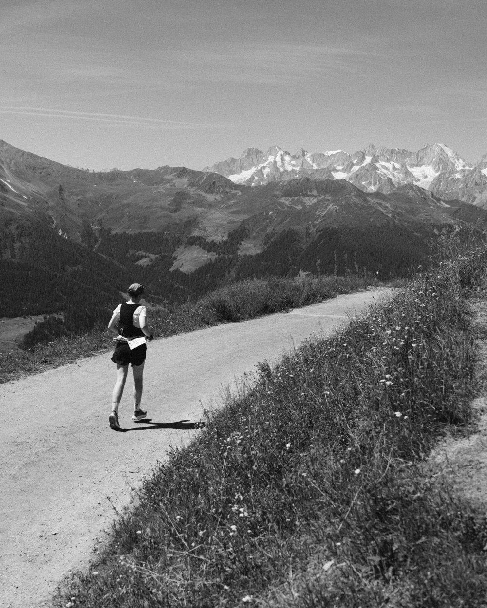 A runner on a gravel road high above a valley, a snow-topped range in the distance