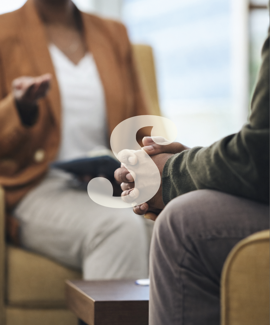 Two people holding hands during a conversation in a cozy room, with one person holding a tablet, and blurred background.