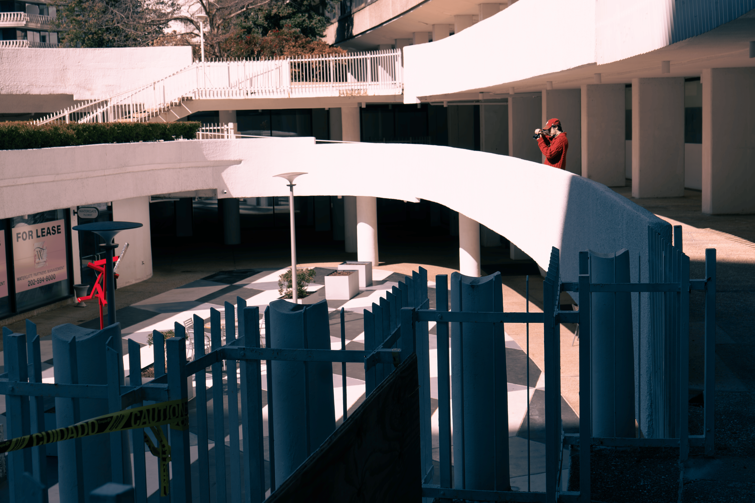 A man in red jacket and cap is taking a photo with camera on an outdoor balcony in Washington DC near the Kennedy Center.