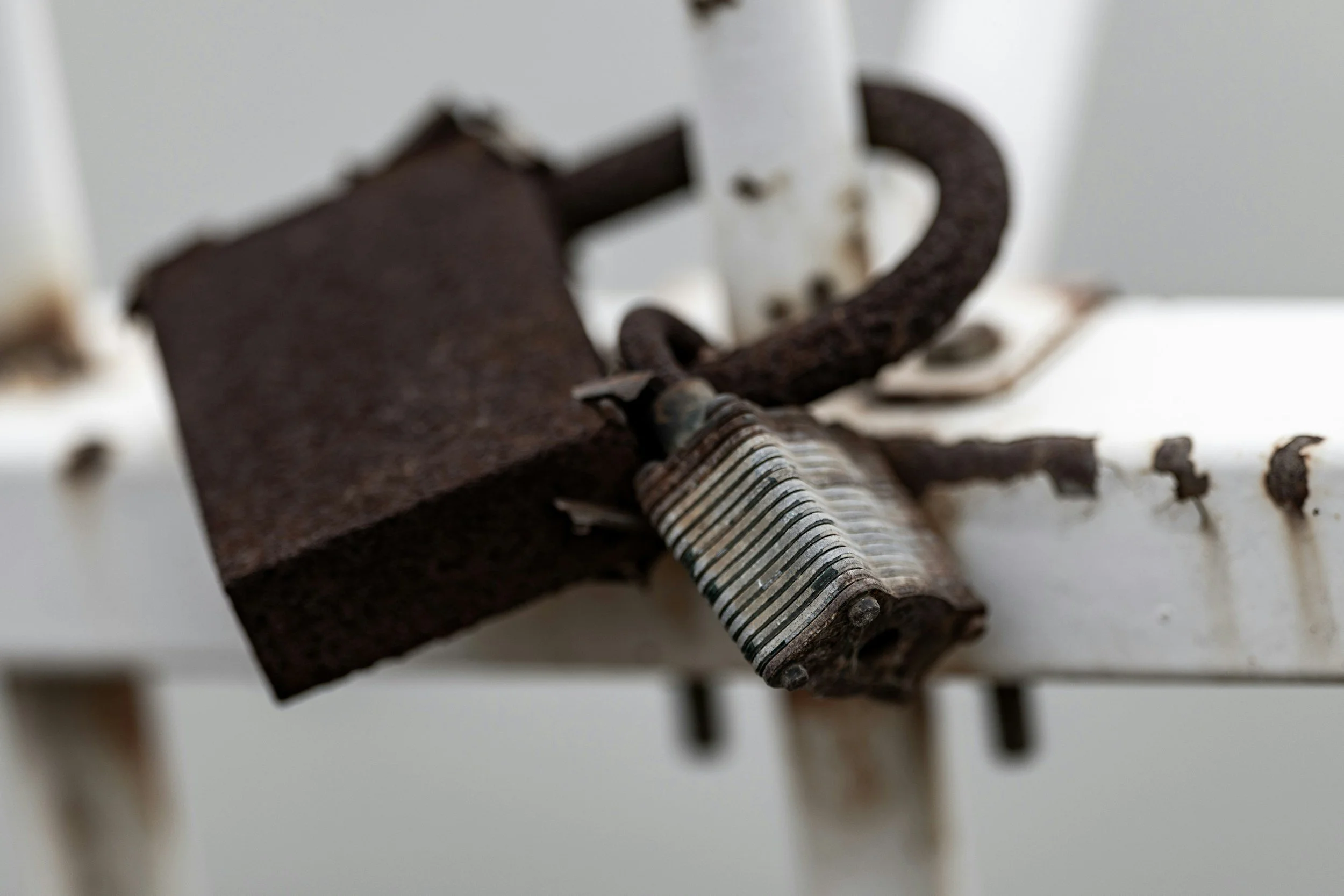 Close-up of a rusty nail bent around a vice grip, set on a white surface with scattered small debris and a blurred white background.
