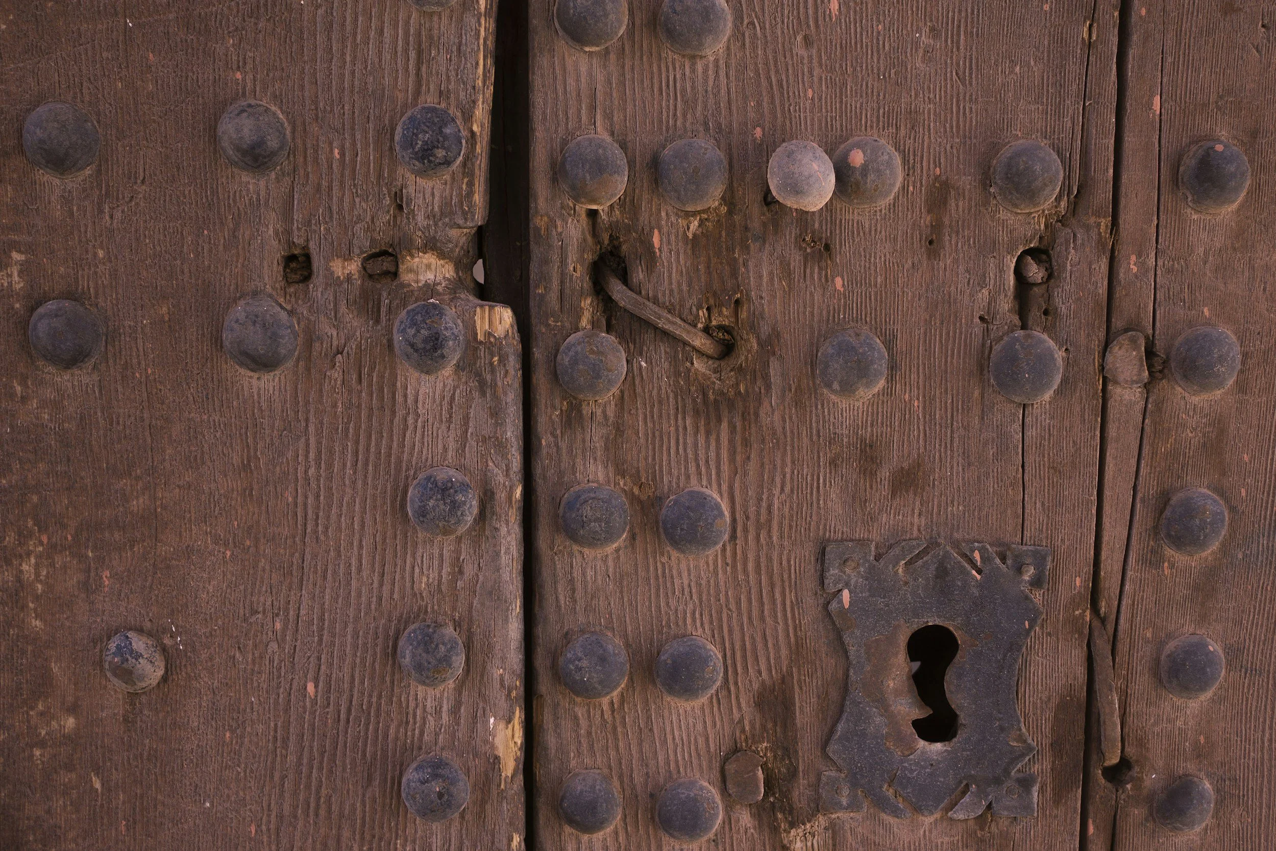 Close-up of weathered wooden door with numerous round metal studs and metal latch.