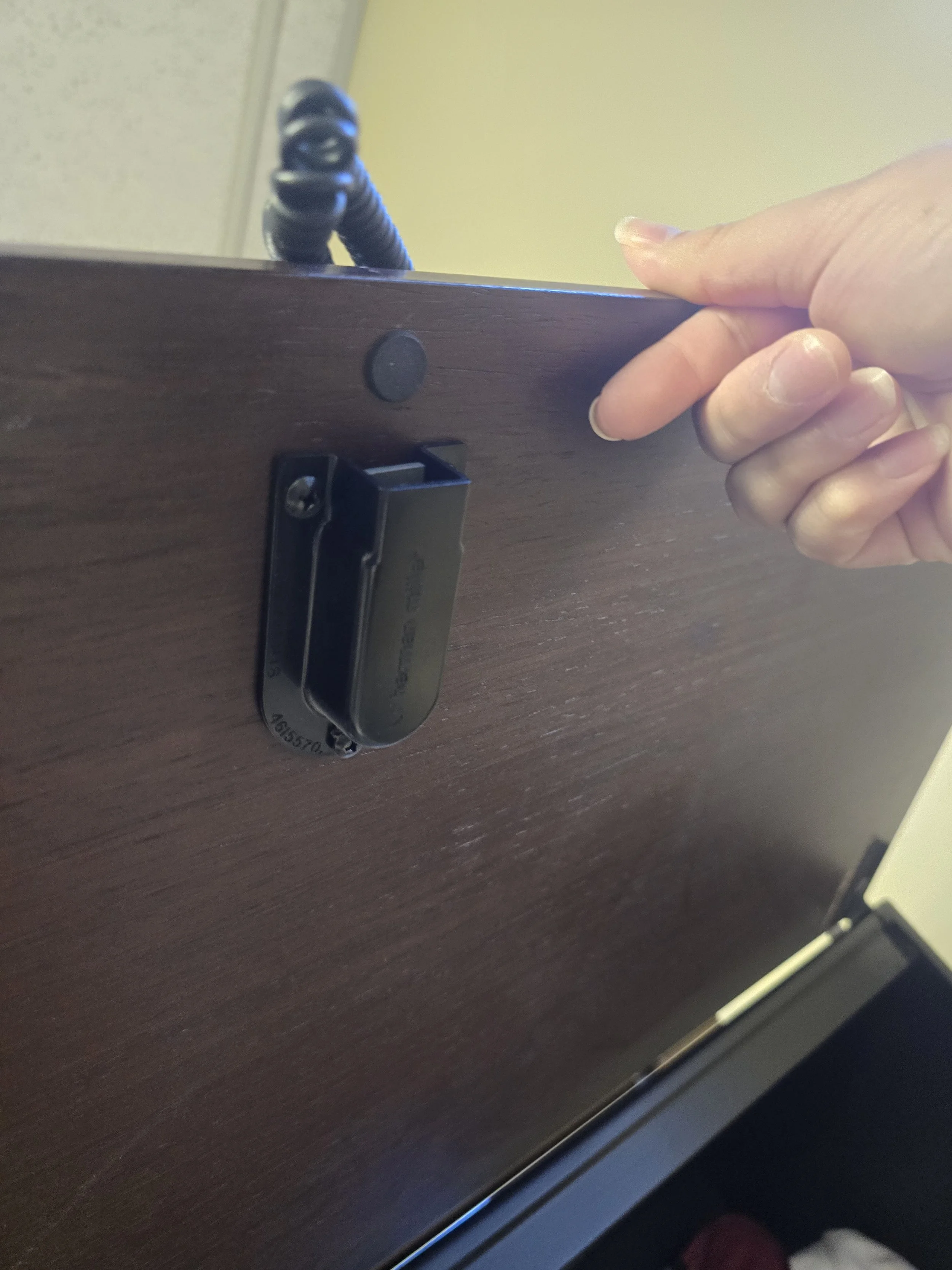 Person's hand adjusting a lock on a wooden desk with a black coiled cable on top.