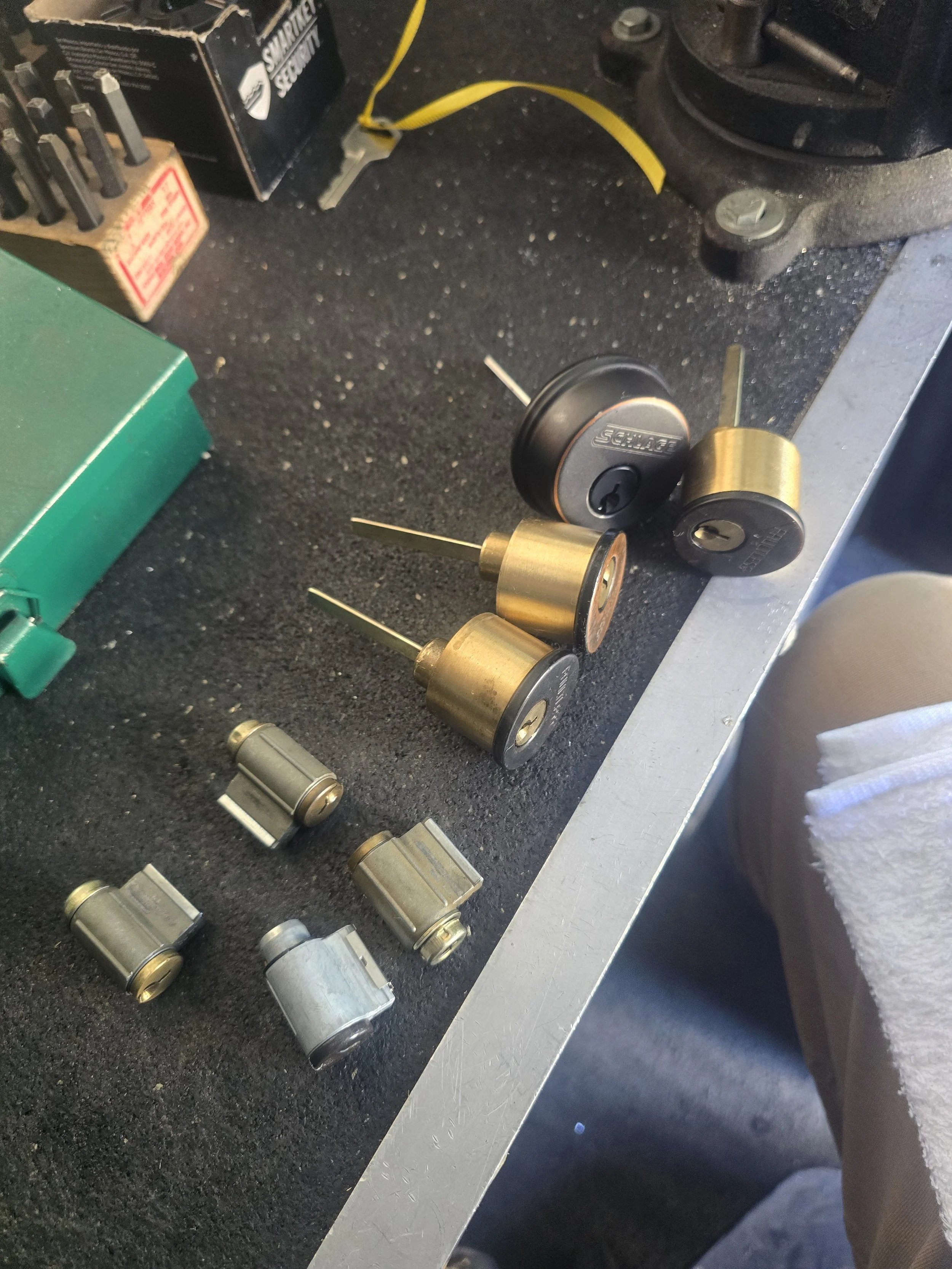 Various locks and lock parts on a workbench, including a pair of brass padlocks, some cylinders, and other lock components.