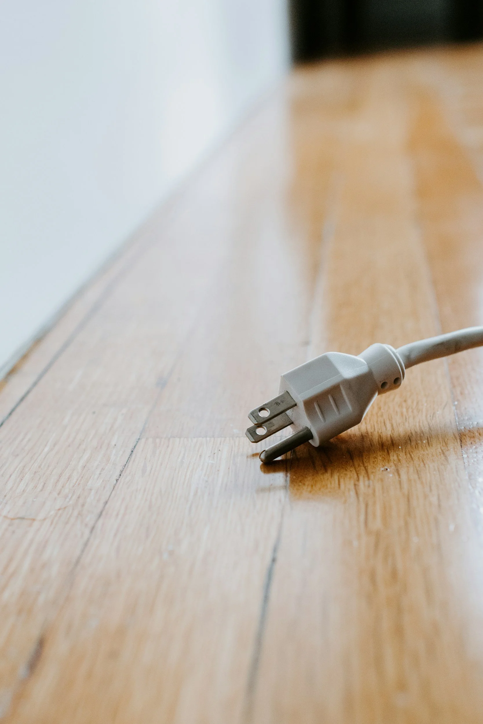 A white electrical power cord and plug on a wooden floor near a white wall.