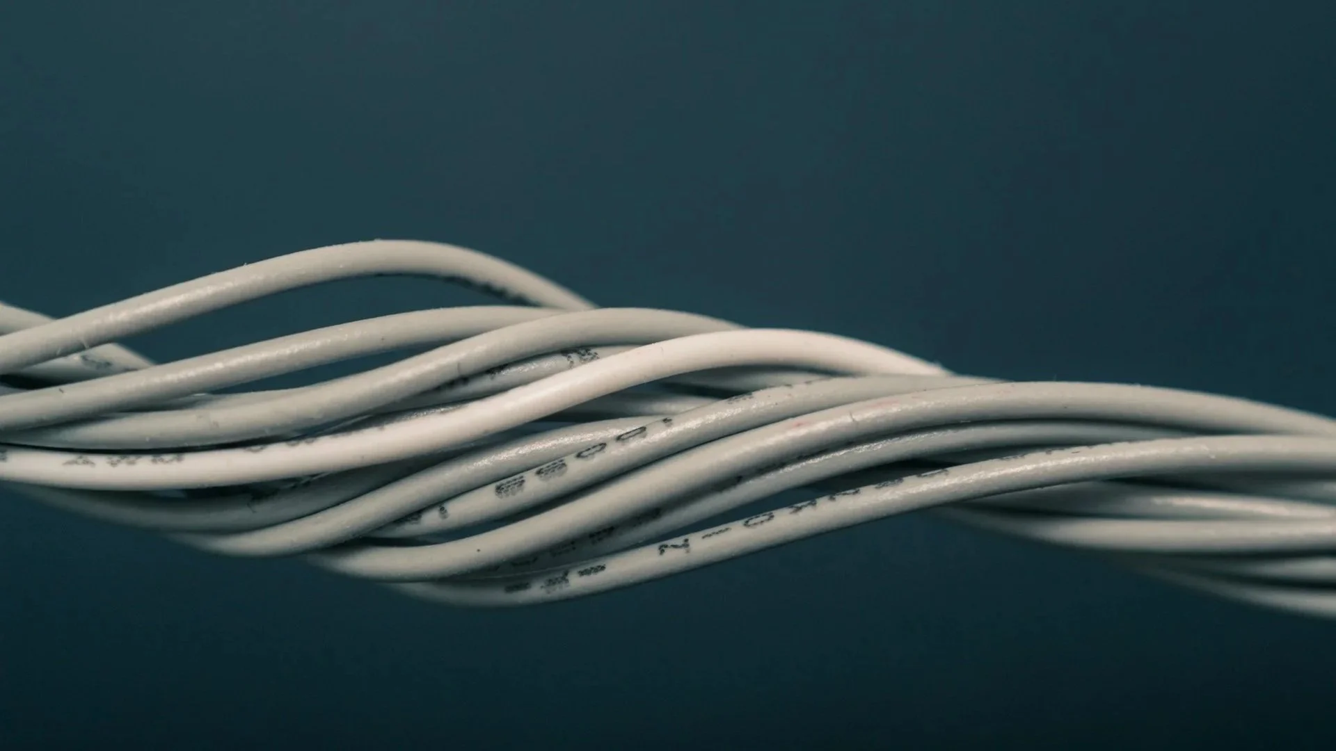 Close-up of white electrical wires twisted together on a dark surface.