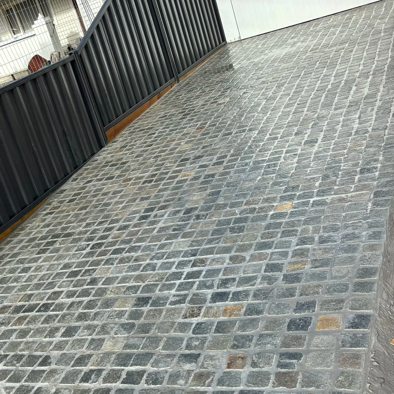 Stone-paved outdoor patio with black metal railing and some wet spots.